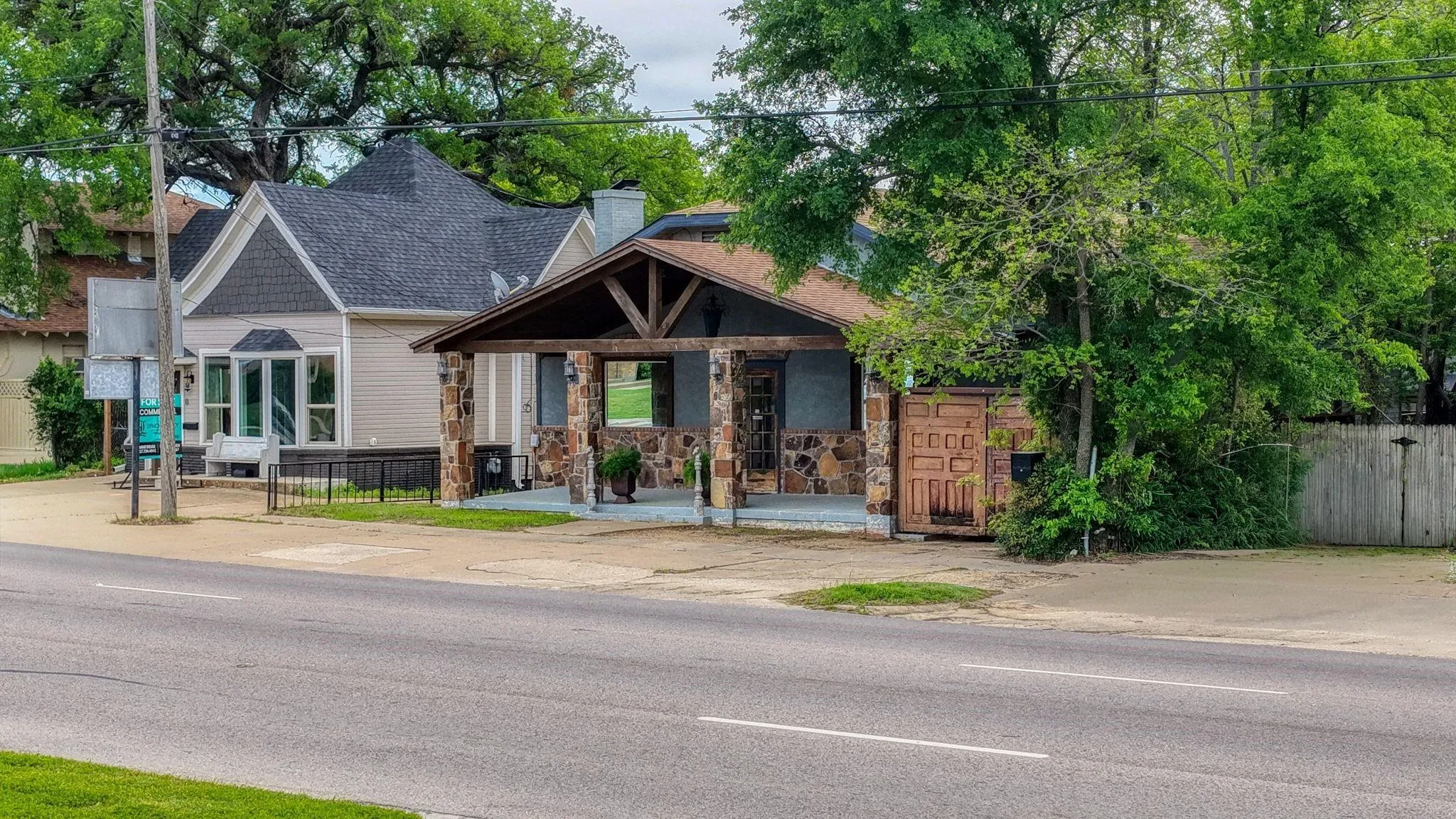 Stone veneer facade with wood structural elements, covered entry, and dark shingle roof
