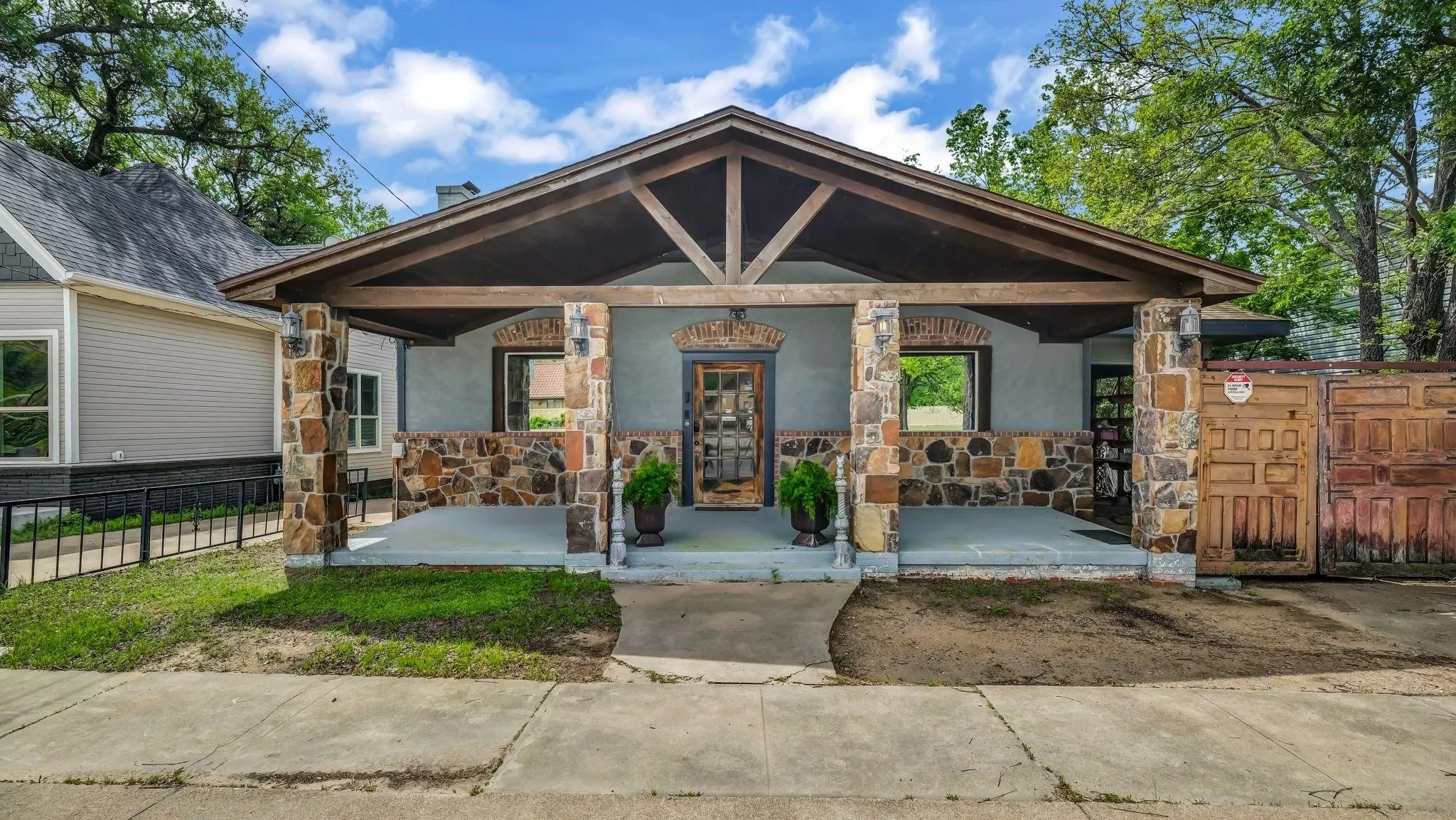 Stone veneer detailing across the facade and columns, expansive covered front porch, exposed wood beam porch ceiling, arched front entry with a wood-finish door, and arched window frames