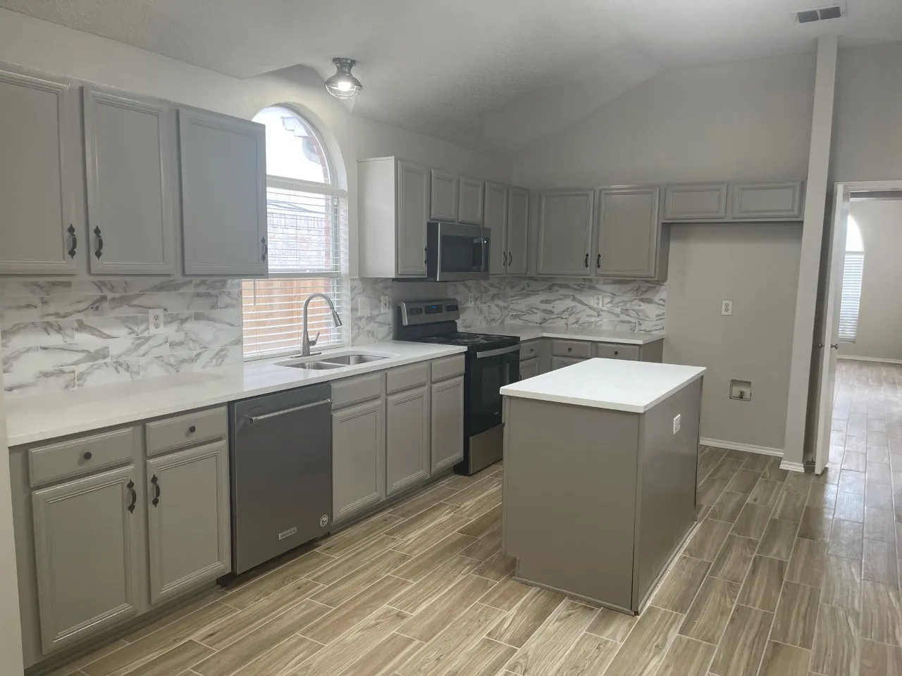 Kitchen featuring a center island, wood-finish flooring, vaulted ceiling, built-in stainless steel appliances, and a tile backsplash