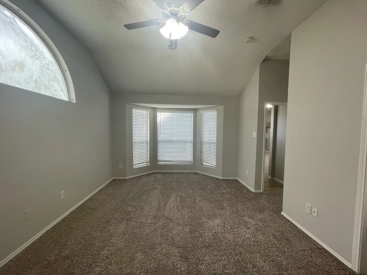 Vaulted ceiling featuring a ceiling fan, bay window with blinds, and an arched window
