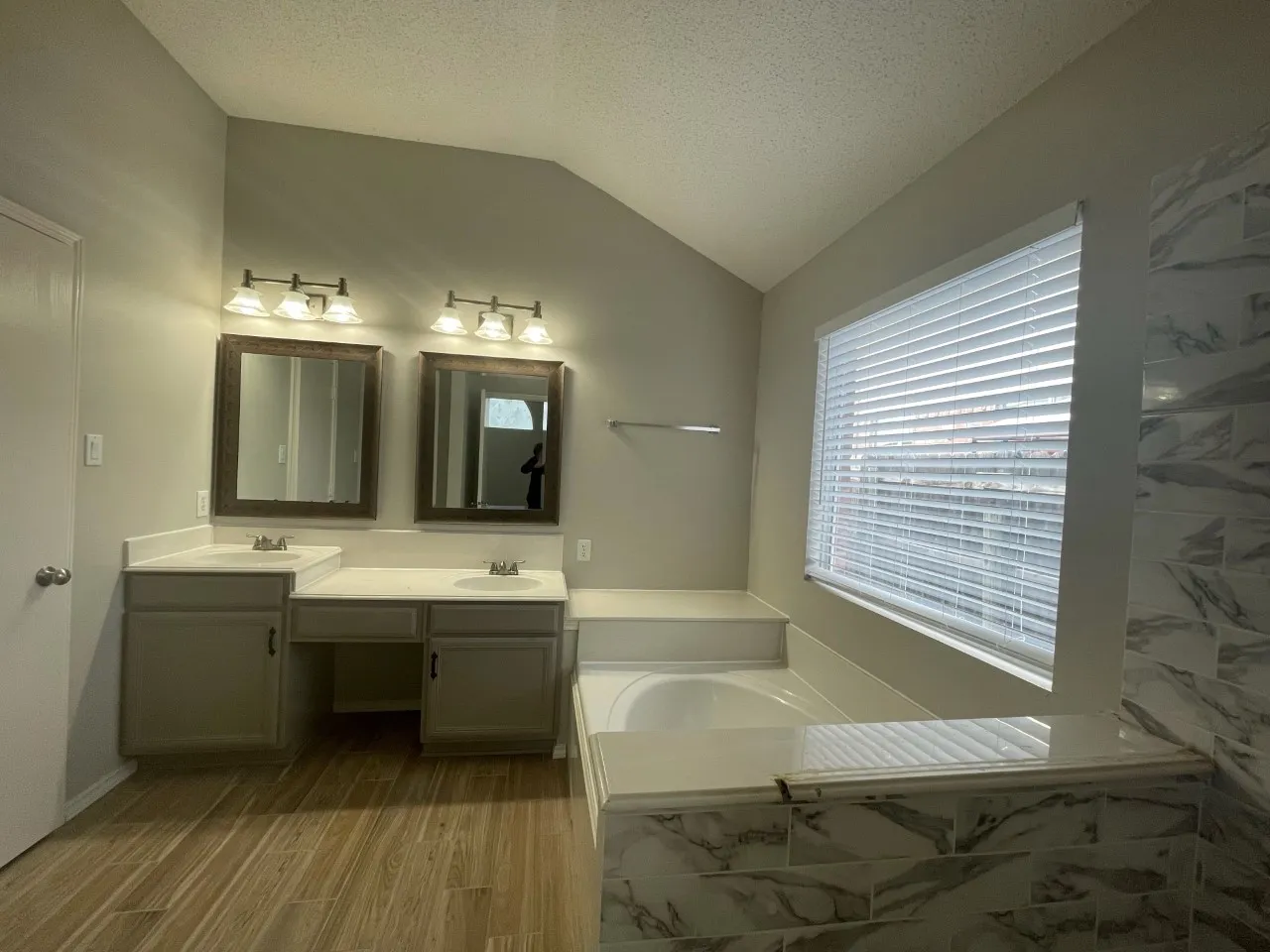 Dual vanity with integrated sinks, wood-finish flooring, built-in soaking tub, and tiled surrounds