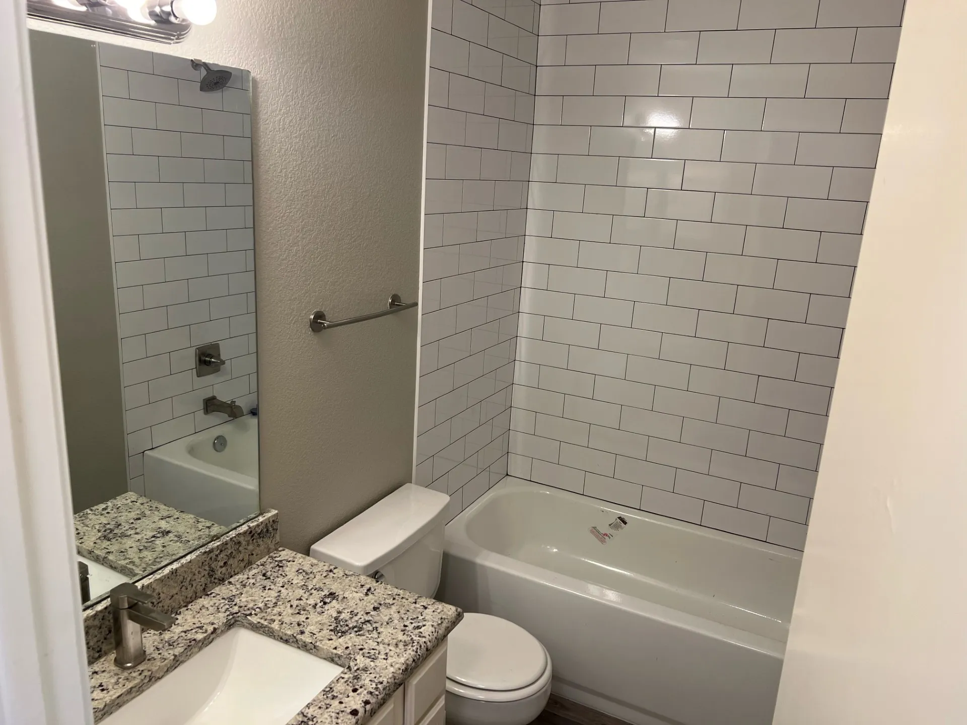 White subway tile shower surround, built-in bathtub, vanity with integrated sink, speckled countertop, and brushed nickel fixtures