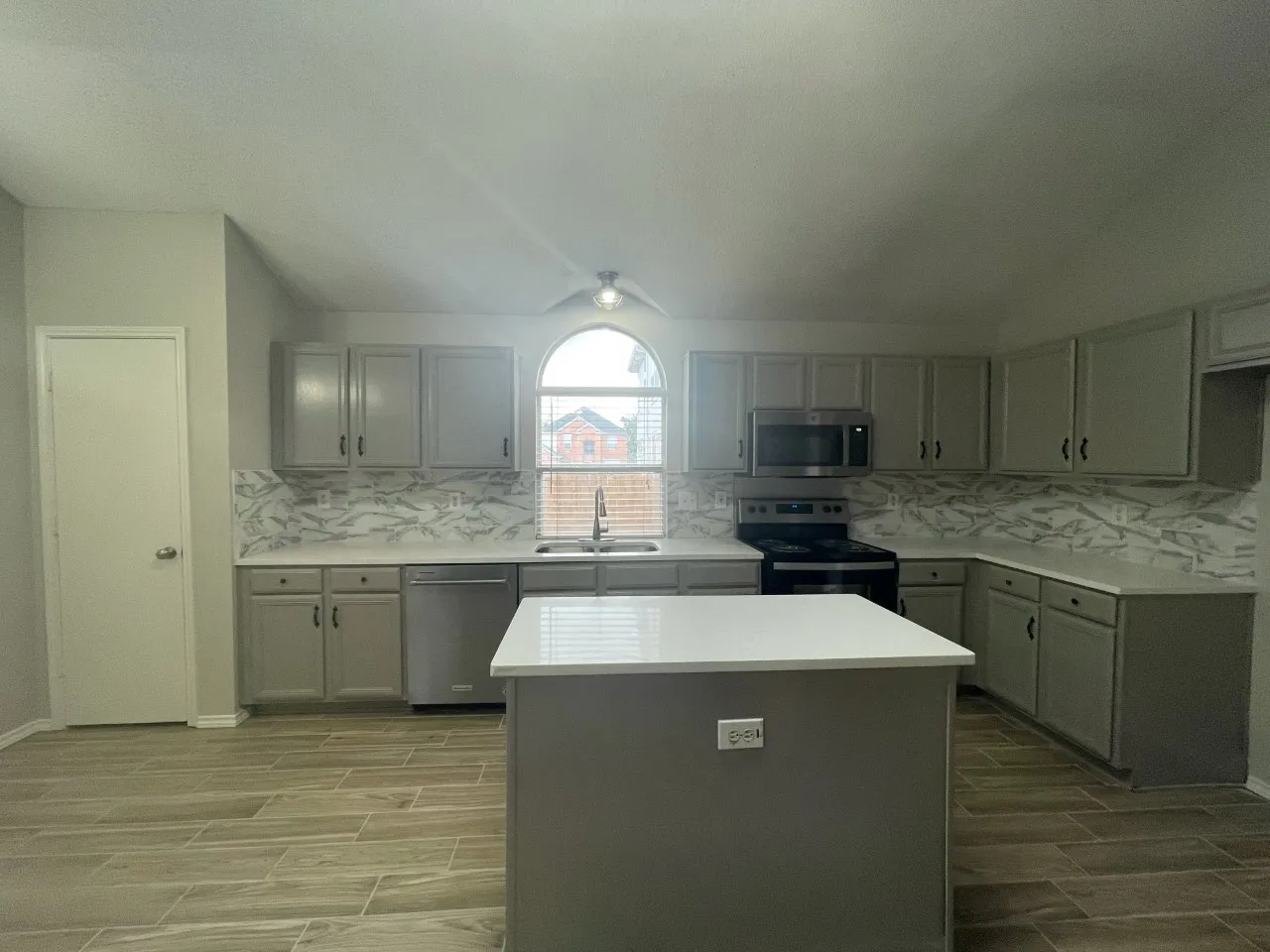 Modern kitchen featuring an arched window, stainless steel appliances, wood-finish flooring, a central island, and extensive cabinetry