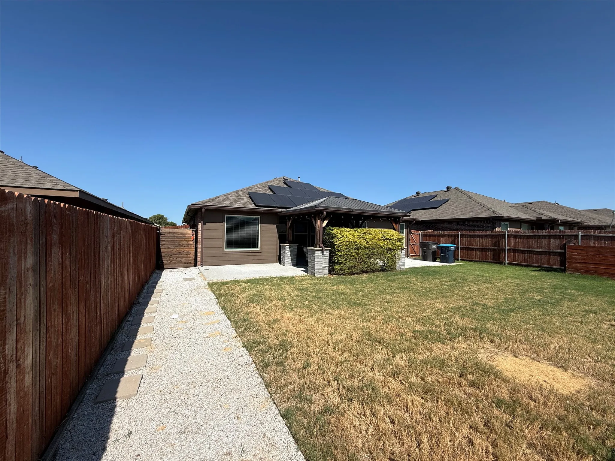 Rear exterior featuring a covered patio, stone column accents, and solar panels