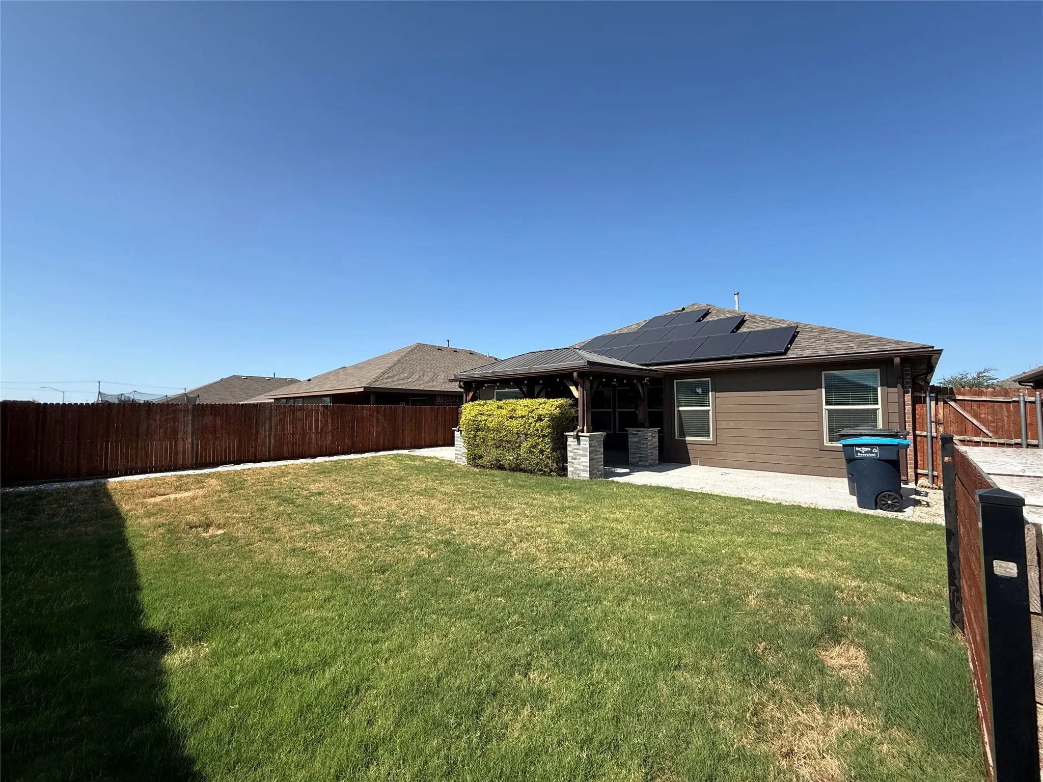 Backyard featuring a privacy fence, covered patio with stone-wrapped columns, exterior siding, and roof-mounted solar panels