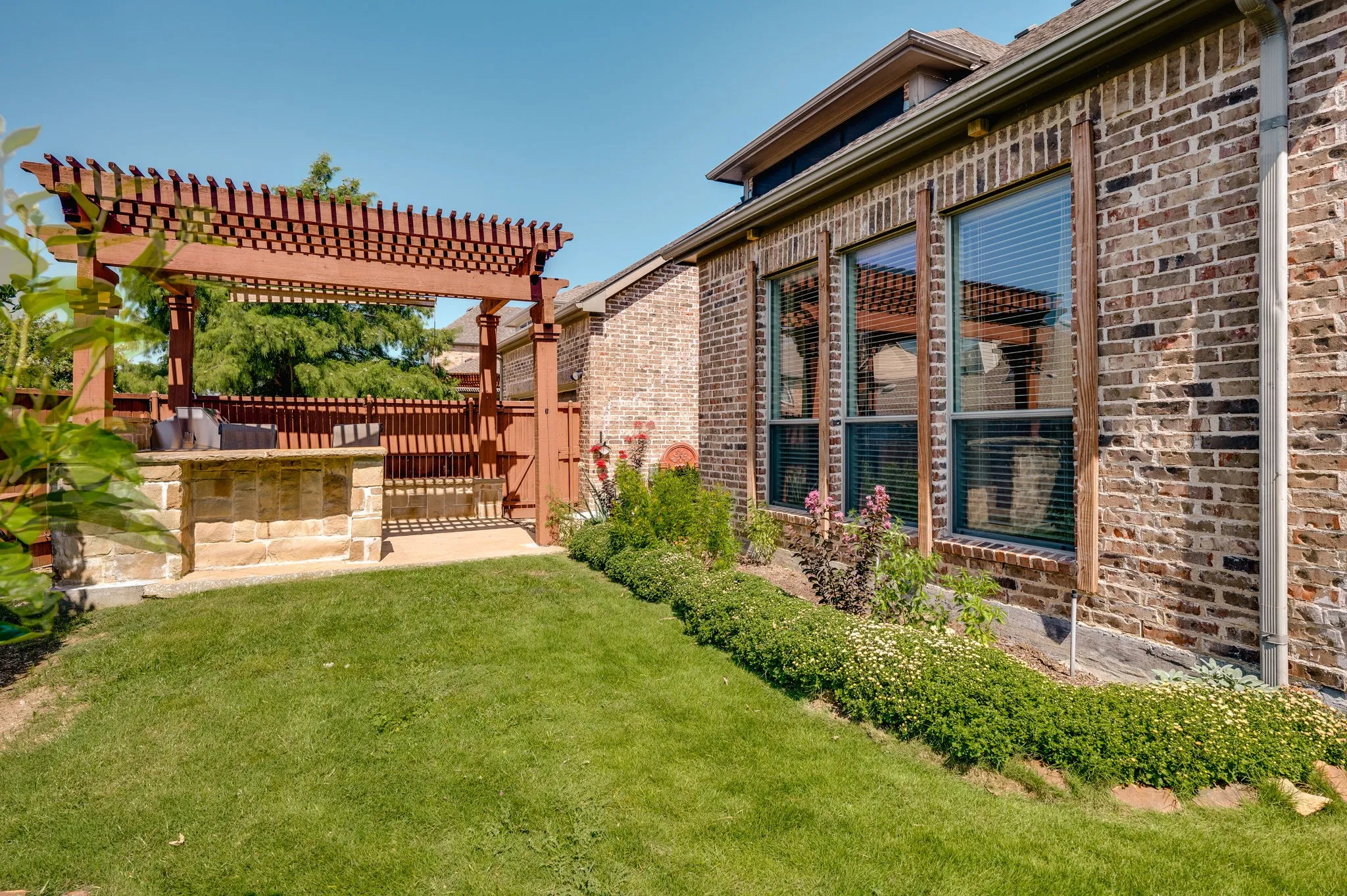 Expansive lawn with a stone-clad outdoor bar and pergola structure, brick exterior, and multiple windows with blinds