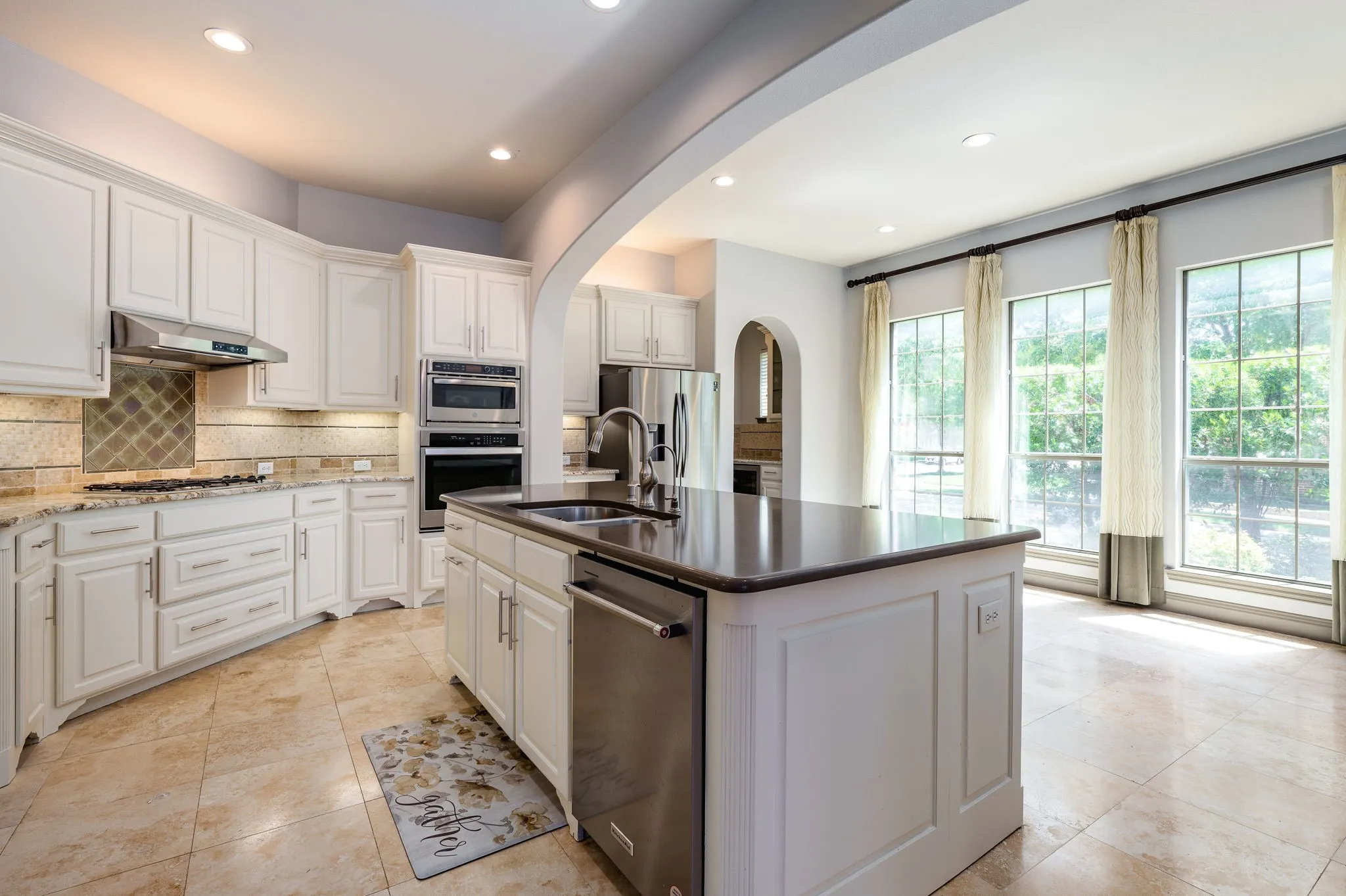 Kitchen featuring white cabinetry, stainless steel appliances, a center island with sink, tile flooring, and arched entryway