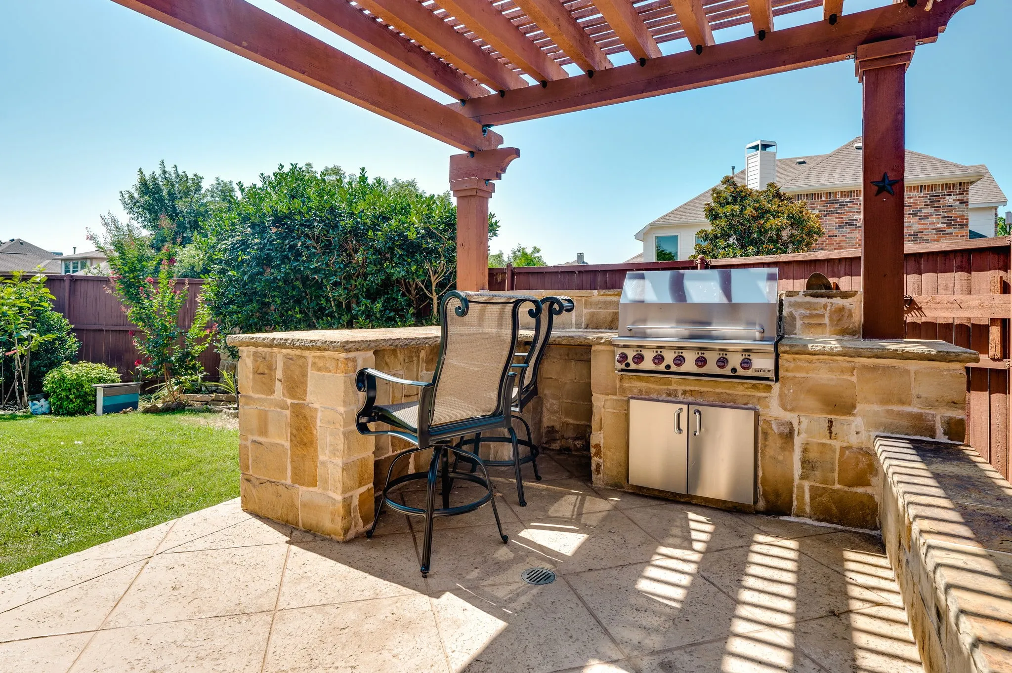 Outdoor kitchen with built-in grill and stainless steel cabinetry, stone-clad bar, and a wood pergola