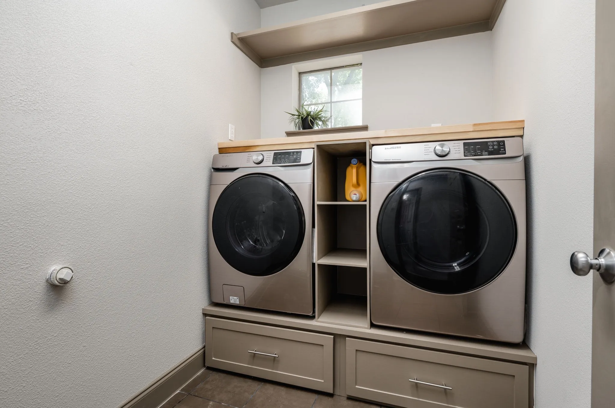 Built-in laundry appliances with wood-finish countertop, shaker-style drawer storage, and integrated shelving