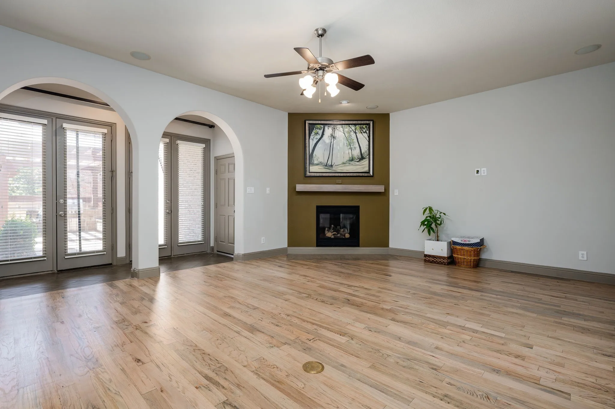 Hardwood-finish flooring, recessed fireplace, arched doorways, ceiling fan, and multiple exterior doors