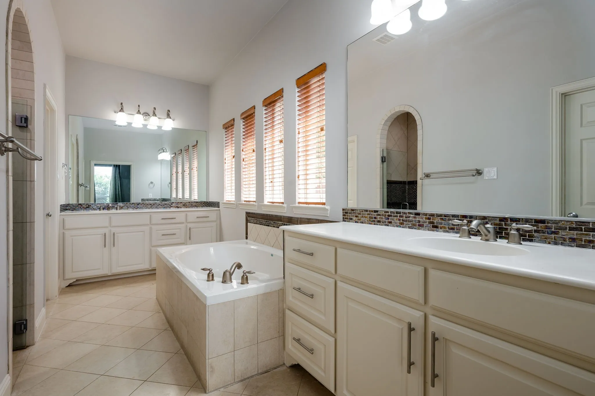 Dual vanity with undermount sinks, integrated soaking tub, tiled flooring, and arched shower enclosure