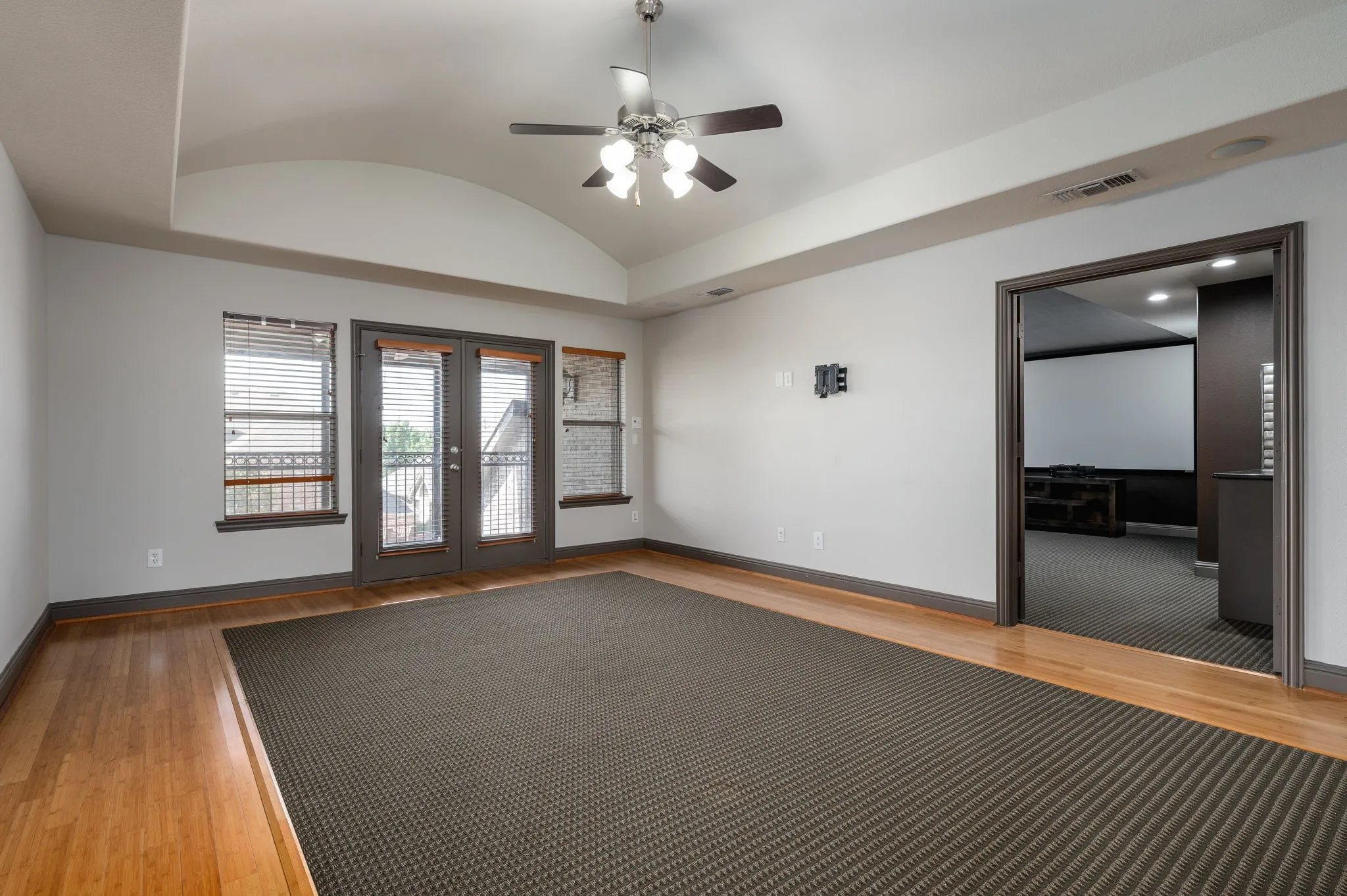 Arch vaulted ceiling with a ceiling fan light fixture, wood-finish flooring, double glass panel doors, and an entertainment room entrance