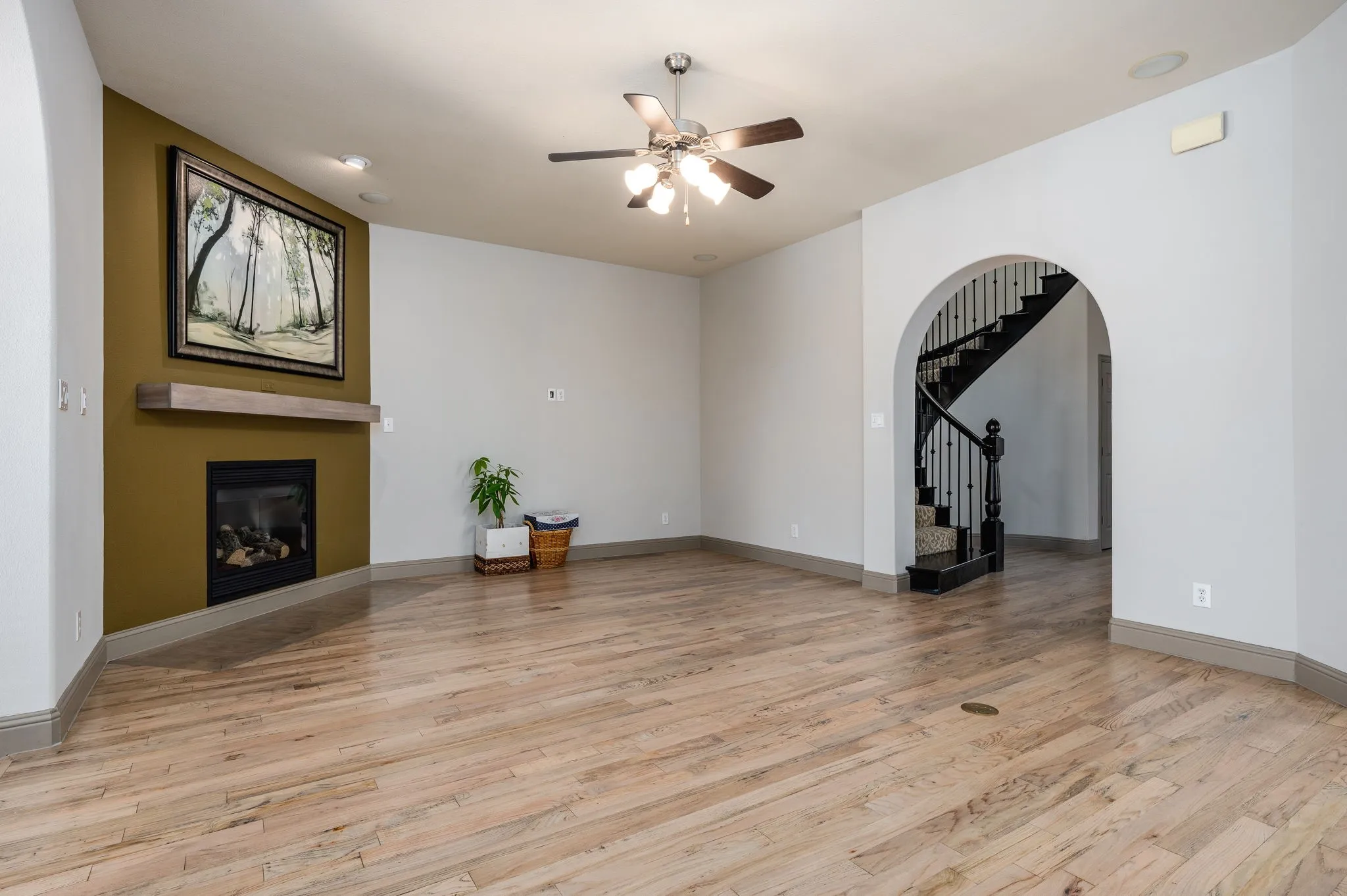 Recessed lighting, wood-finish flooring, built-in fireplace with floating mantel, ceiling fan with light kit, and an arched entryway