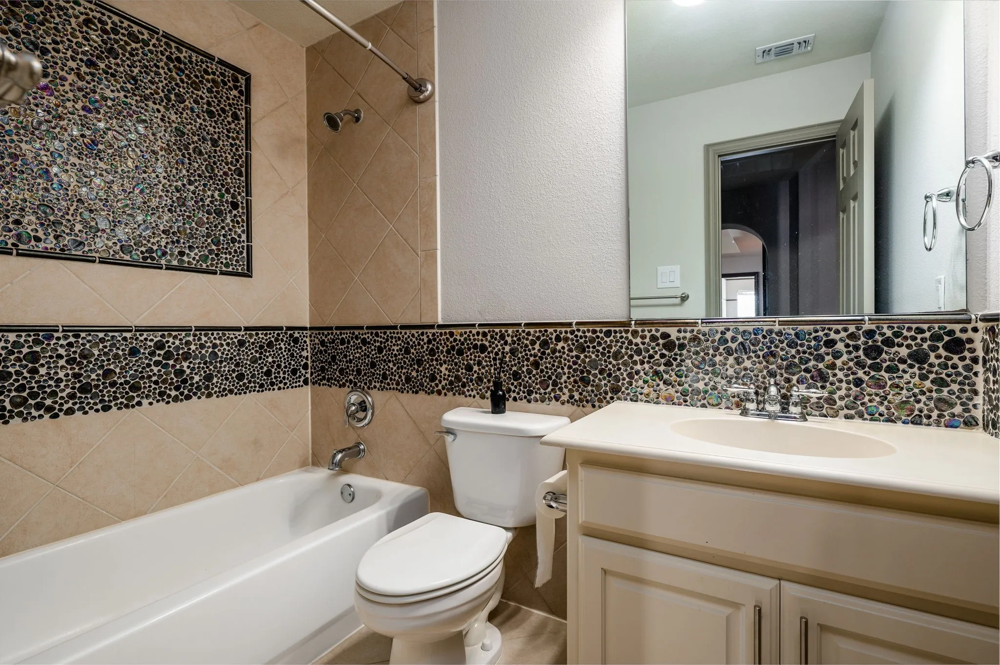 Bathroom with a built-in bathtub, a toilet, a vanity with an integrated sink, and decorative tile accents