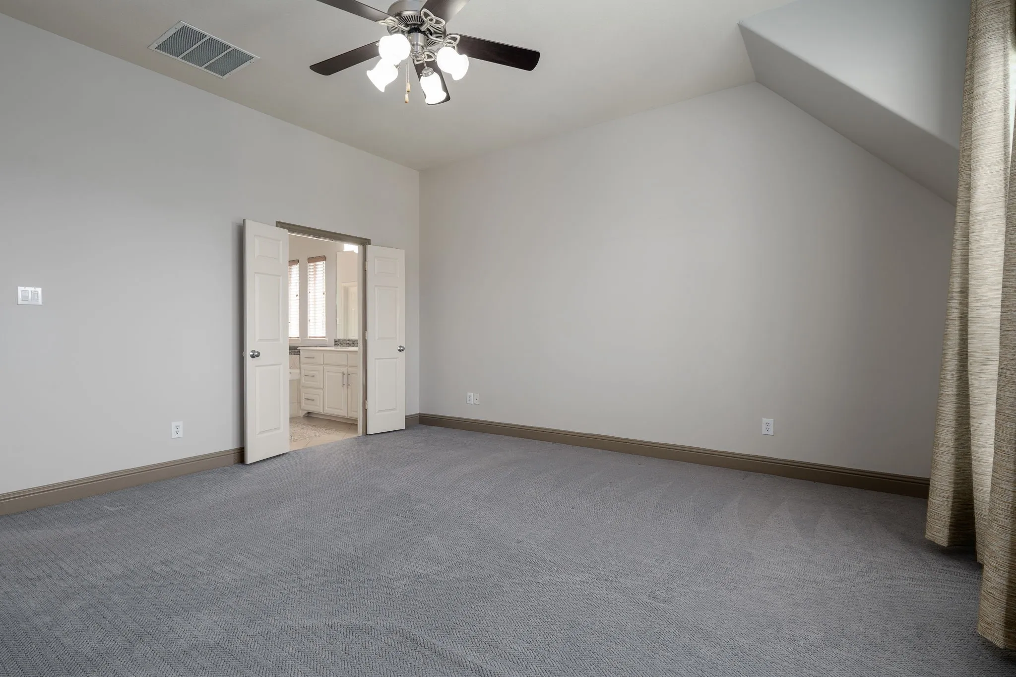 Spacious room with gray textured carpeting, a ceiling fan with integrated lighting, and an angled ceiling detail