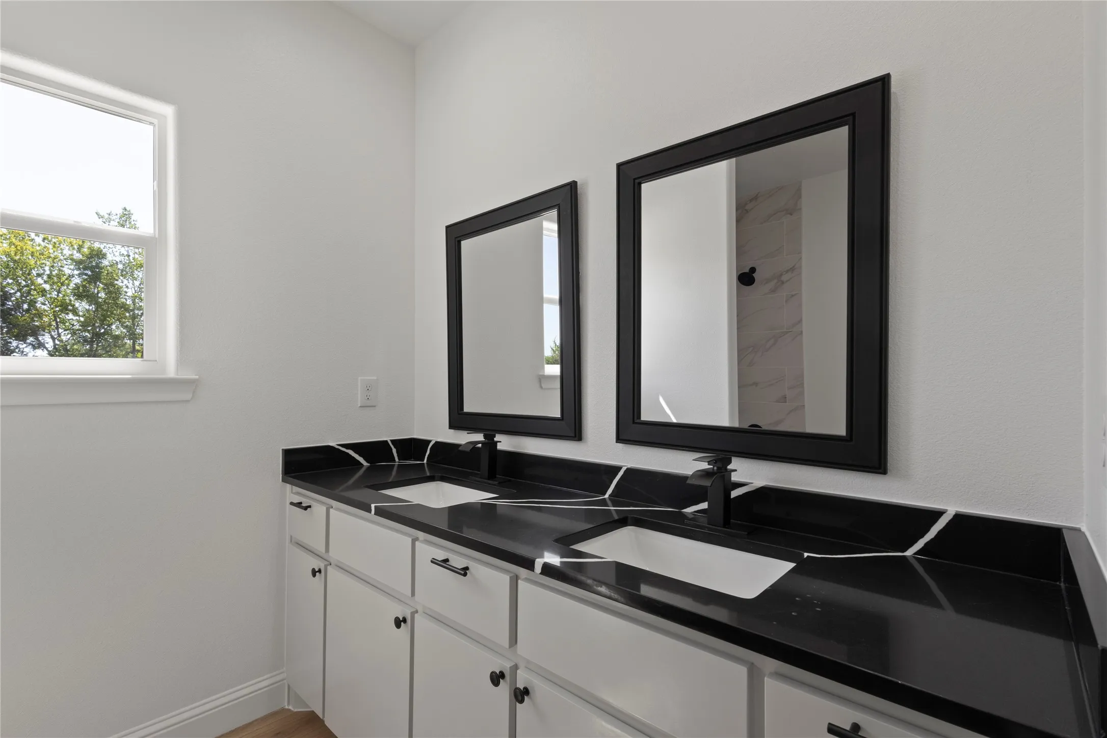 White subway tile shower surround with integrated niche, white bathtub, dual vanity with black countertops, undermount sinks, and black-framed mirrors