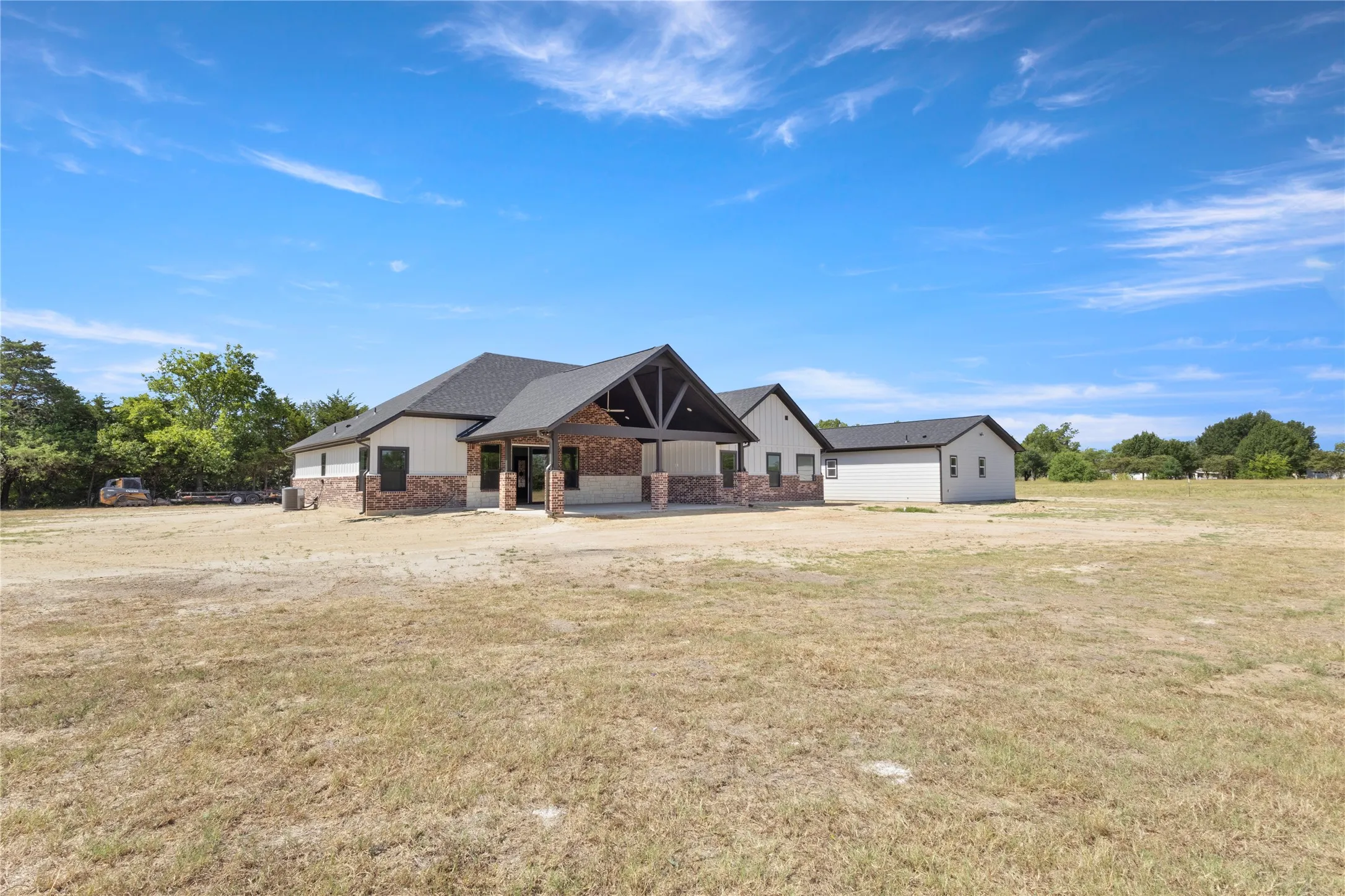 Expansive rural property featuring a custom-built residence with pitched rooflines, stone and stucco exterior, and a covered front porch