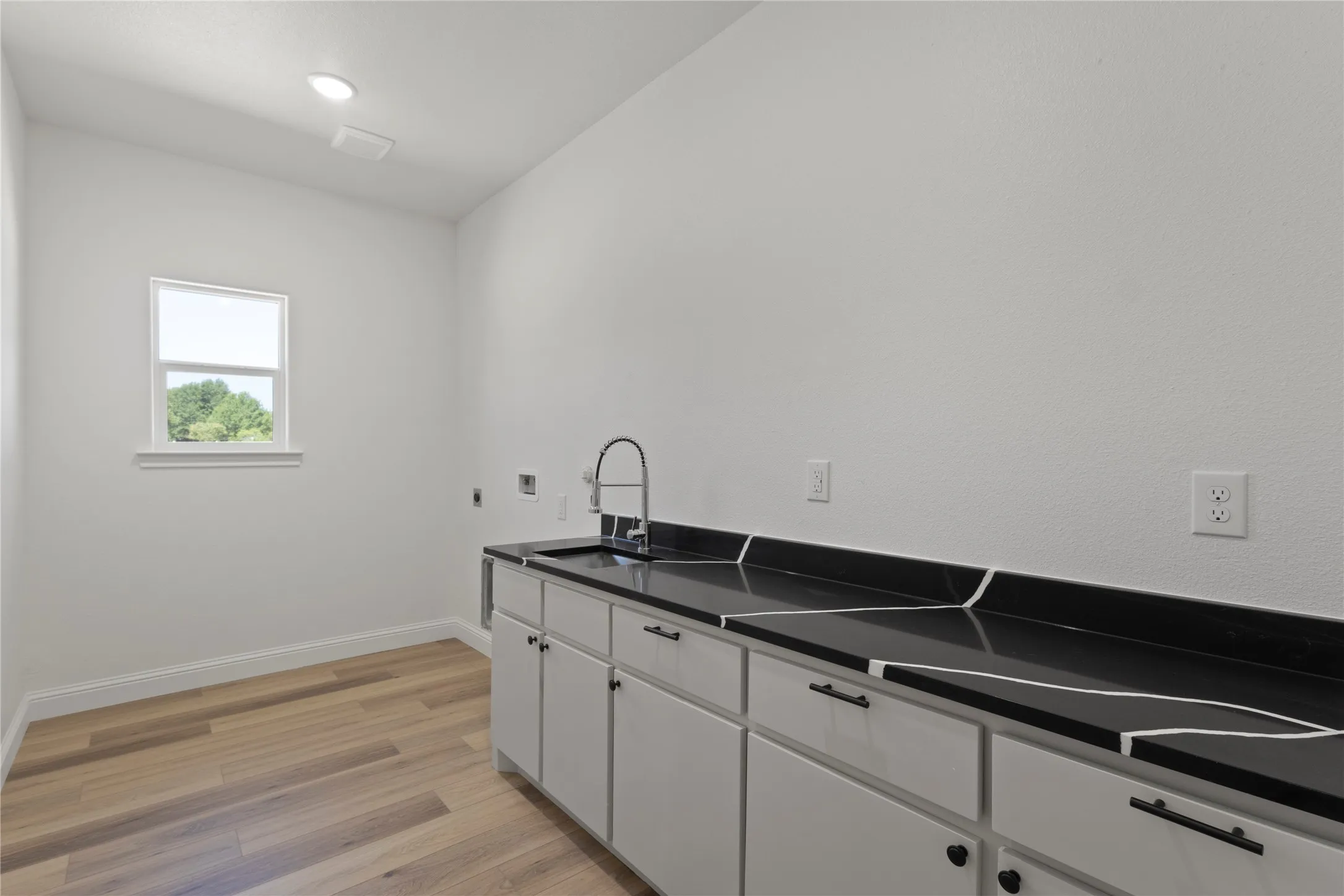 Dual vanity with black countertops and undermount sinks, wood-finish flooring, freestanding soaking tub, and a built-in storage cabinet