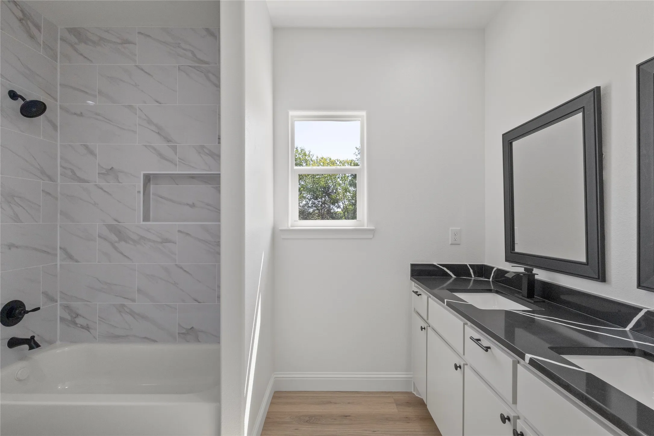 Spacious bathroom featuring a glass-enclosed shower with a rain shower head and a built-in niche, a freestanding soaking tub, a double vanity with ample storage, and wood-finish flooring