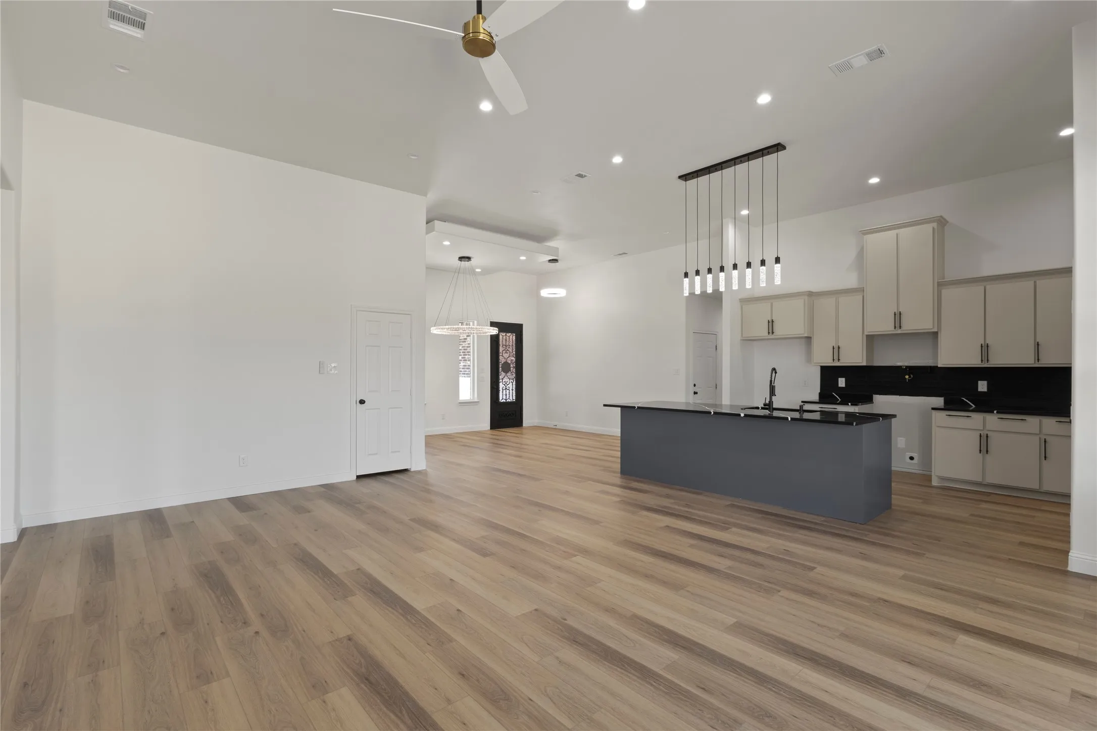 Kitchen featuring light-toned cabinetry, dark countertops with distinctive white veining, a black subway tile backsplash, and wood-finish flooring