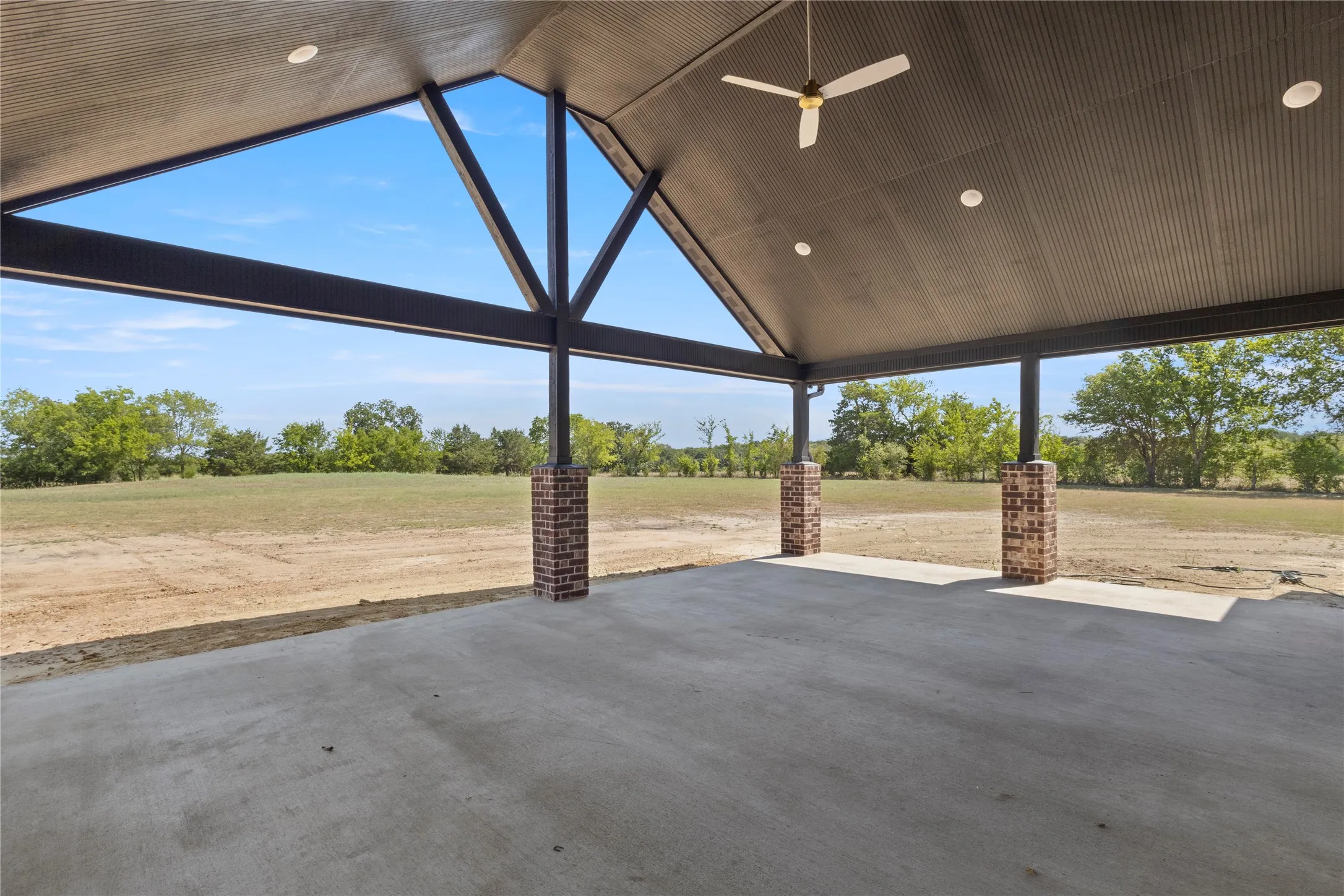 Expansive covered patio featuring a vaulted ceiling with exposed beams, recessed lighting, ceiling fan, and brick-clad support columns