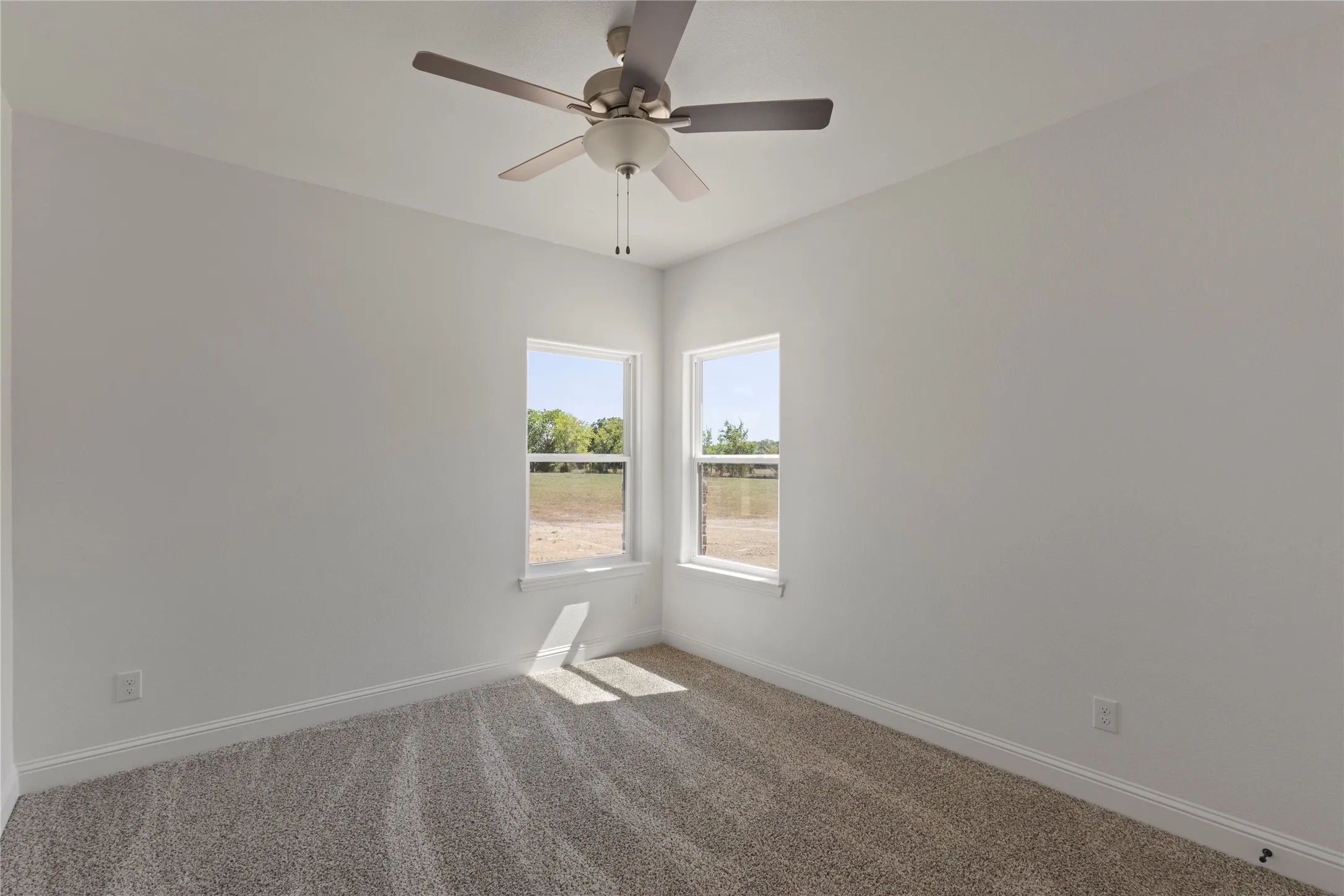 Expansive property featuring a newly constructed residence with an attached garage and a detached accessory structure, surrounded by open fields and mature tree lines