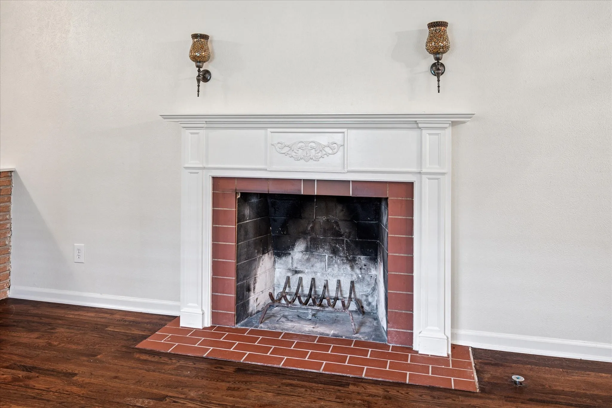 iving room woodburning fireplace with mantle, sconces, brick hearth, and gas starter.