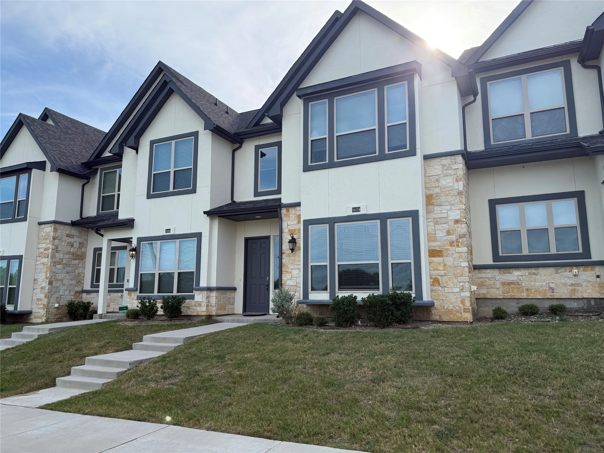 Contemporary facade with stone veneer accents, dark trim windows, gabled rooflines, and a dark entry door