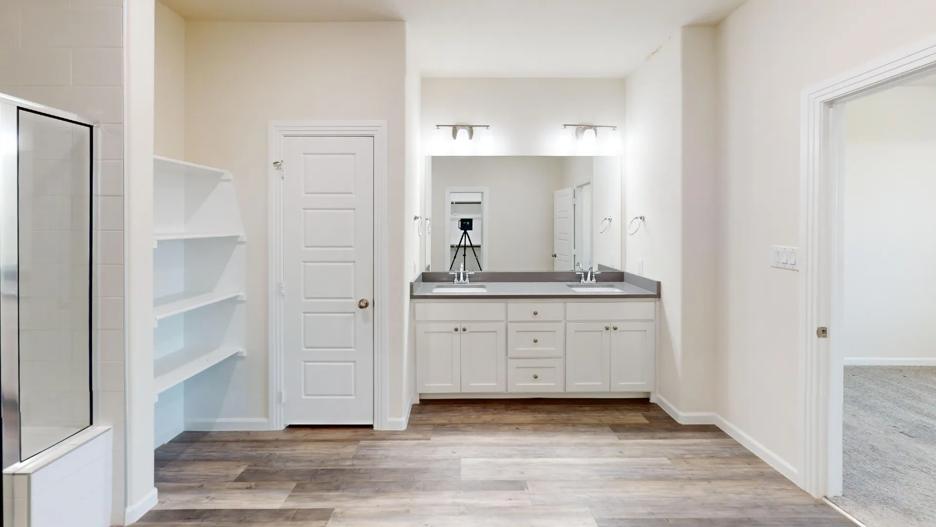 Dual vanity with undermount sinks, wood-finish flooring, built-in shelving, white cabinetry, and a framed shower with clear glass