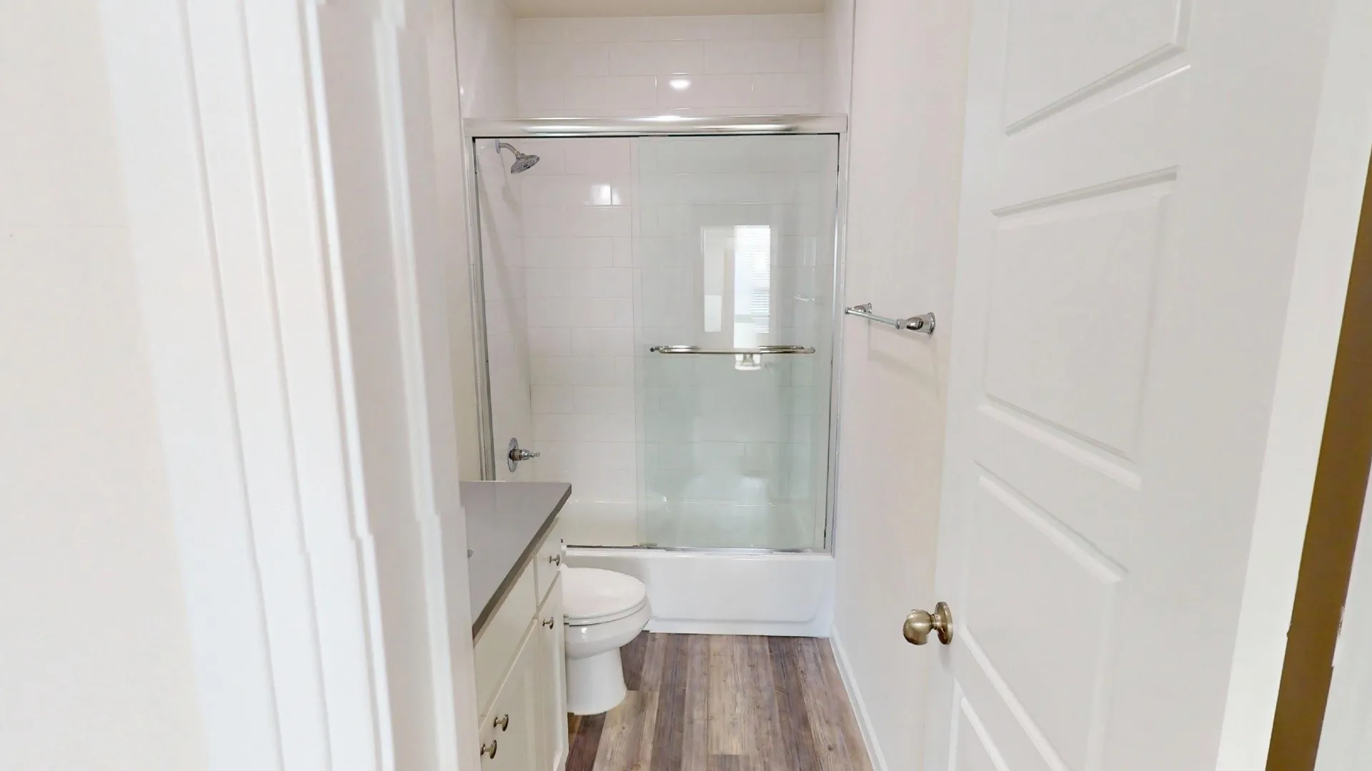 Modern bathroom featuring a frameless glass shower enclosure with chrome hardware, floating vanity with integrated sink and storage, wood-finish flooring, and recessed ceiling lighting