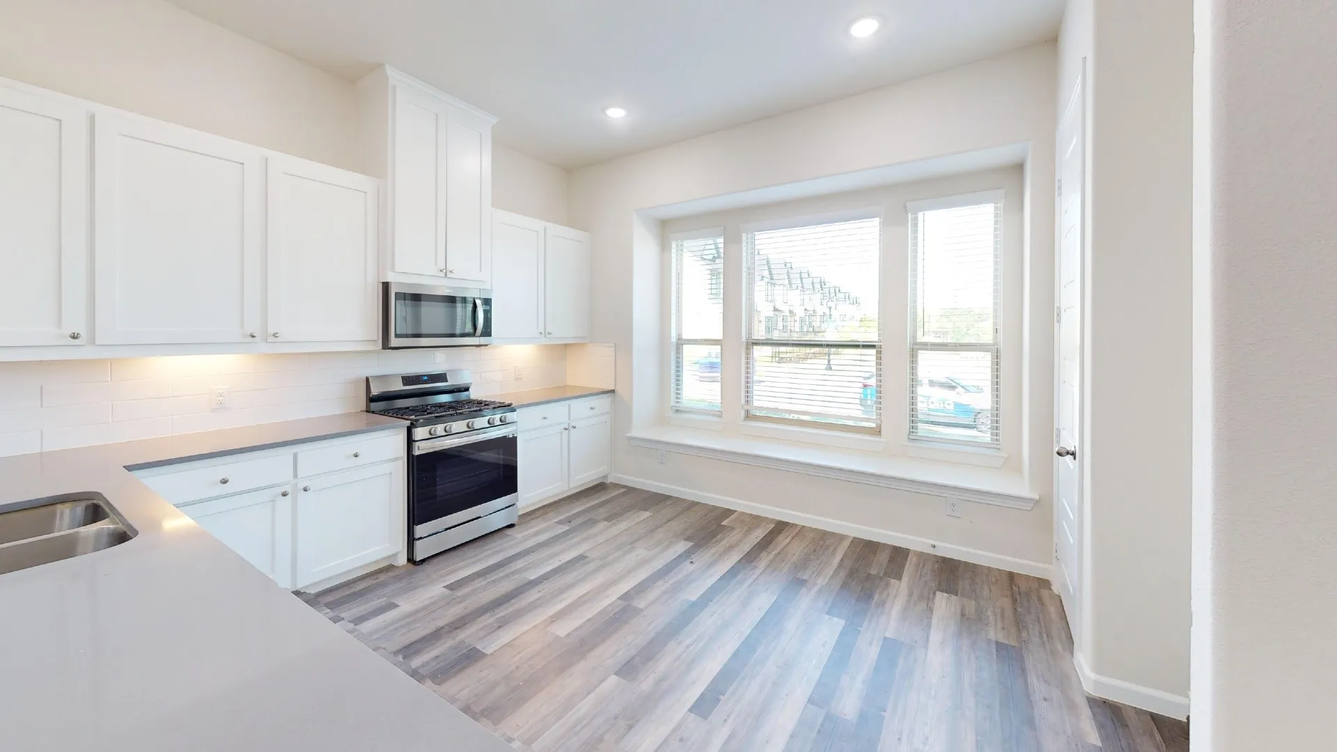 Contemporary kitchen featuring white cabinetry, stainless steel appliances, light gray countertops, and wood-finish flooring