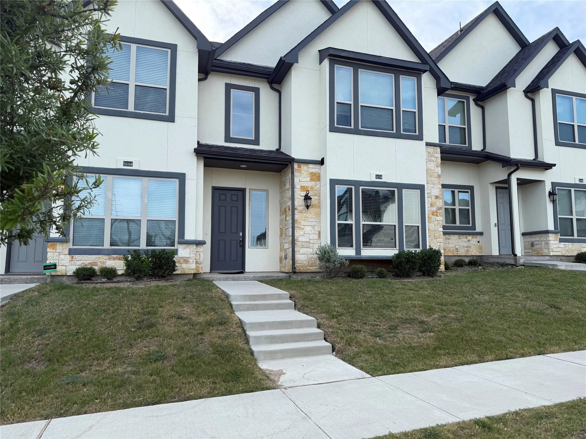 Contemporary townhome exterior featuring light-colored stucco, stone accents, and dark-framed windows