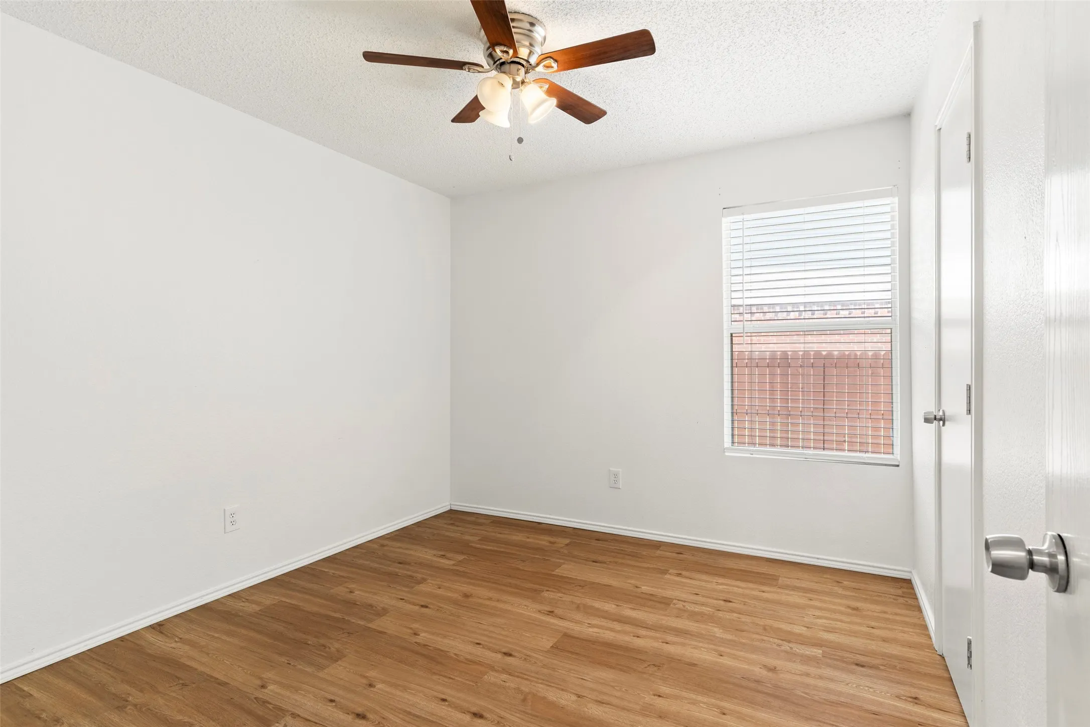 Wood-finish flooring, ceiling fan with integrated lighting, white interior door with brushed nickel hardware, and window with horizontal blinds