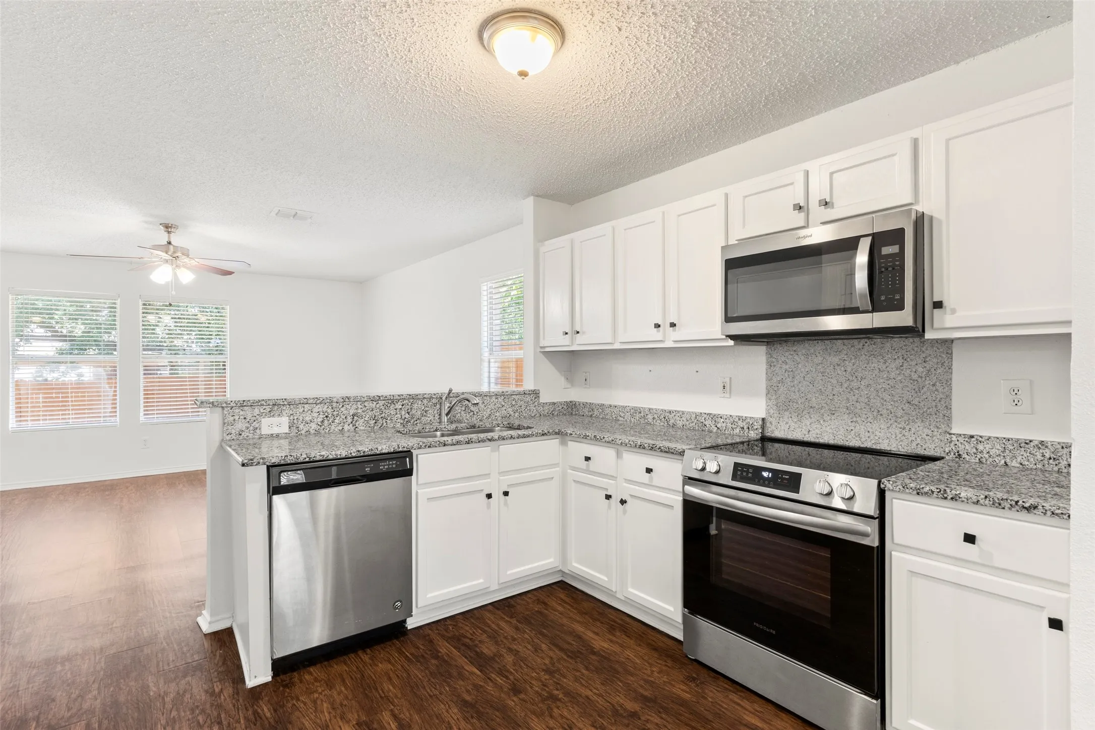 White cabinetry, stainless steel appliances, speckled stone countertops, wood-finish flooring, and a ceiling fan