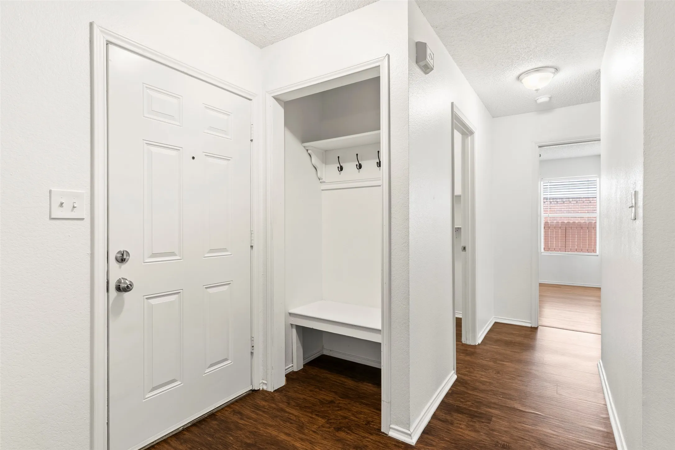 Bright, open entryway featuring rich wood-finish flooring, white six-panel entry door with hardware, and abundant natural light