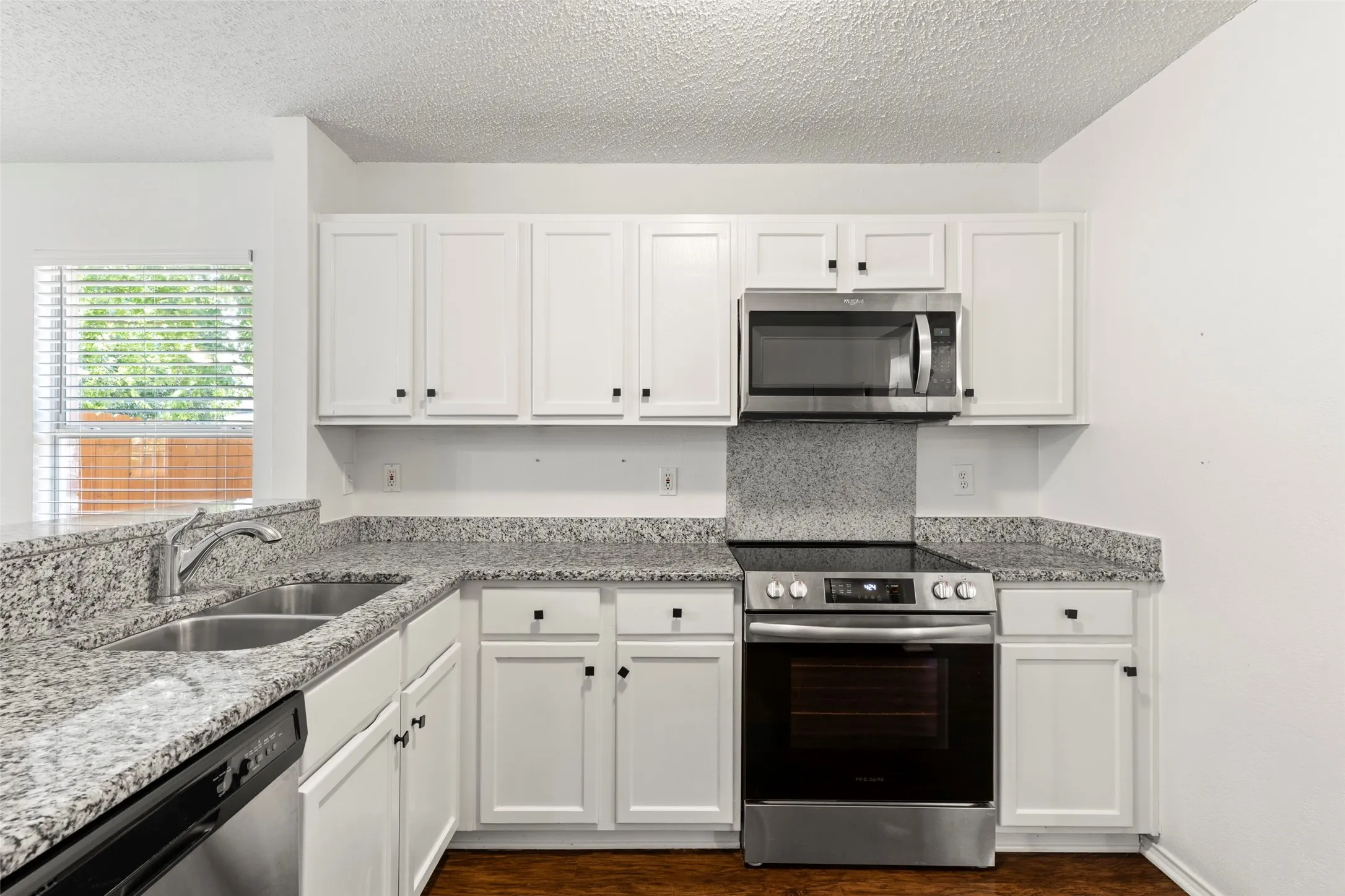 White cabinetry with black hardware, stone-finish countertops, stainless steel appliances, stainless steel double basin sink, and wood-finish flooring