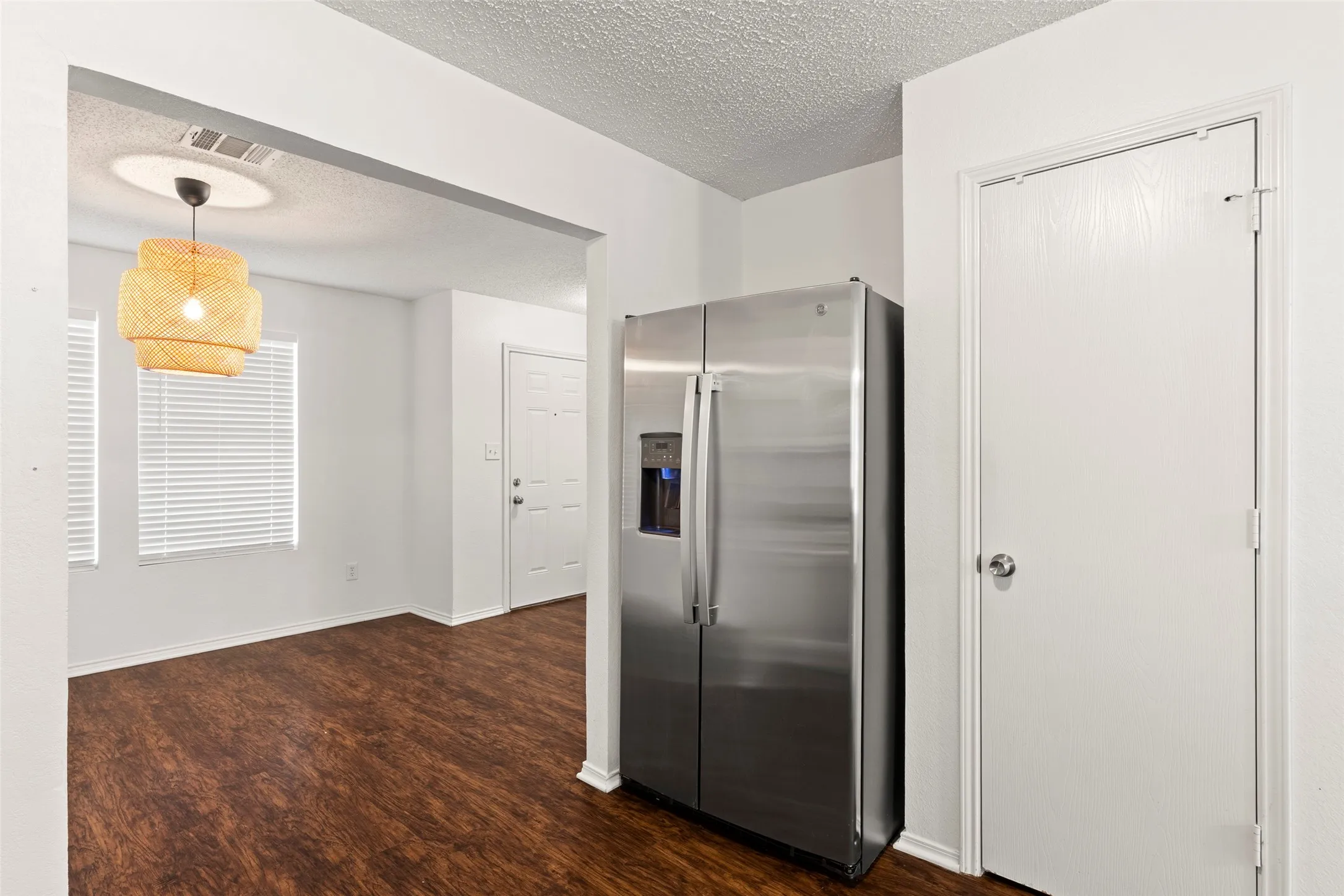 Stainless steel refrigerator, wood-finish flooring, and a decorative pendant light fixture