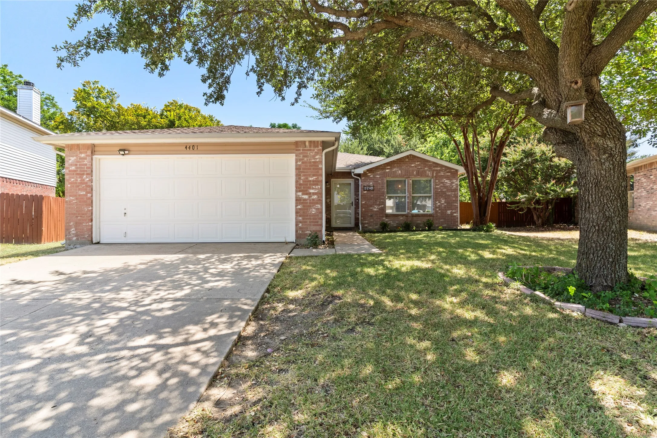 Brick exterior with a two-car garage, concrete driveway, and established front landscaping