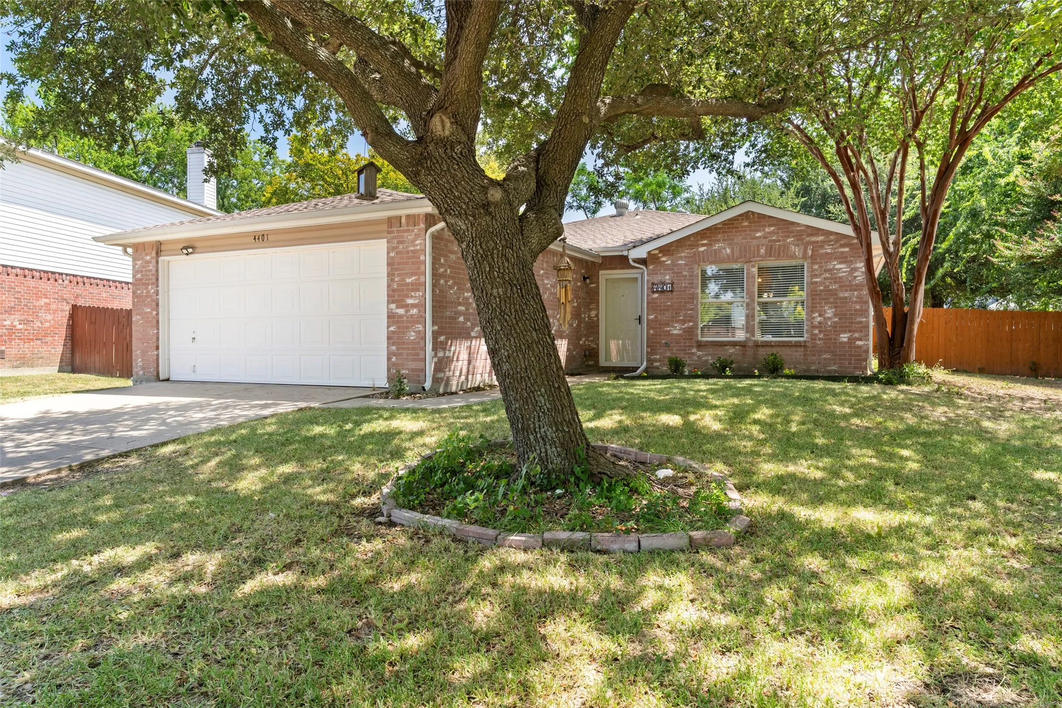 Brick exterior, attached garage, paved driveway, mature trees, landscaped front yard