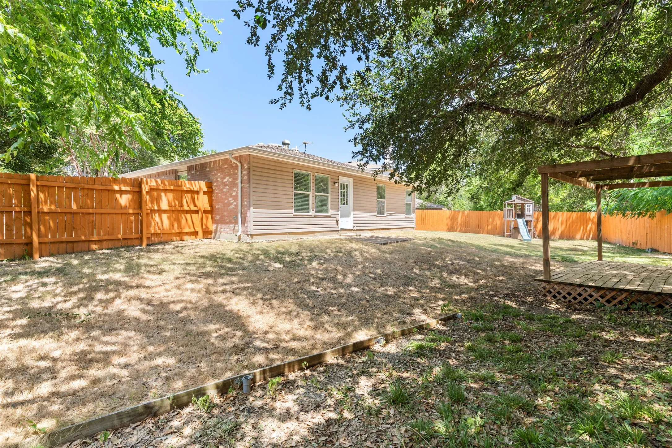 Expansive backyard featuring a wood pergola with a lattice base, a privacy fence, and mature trees