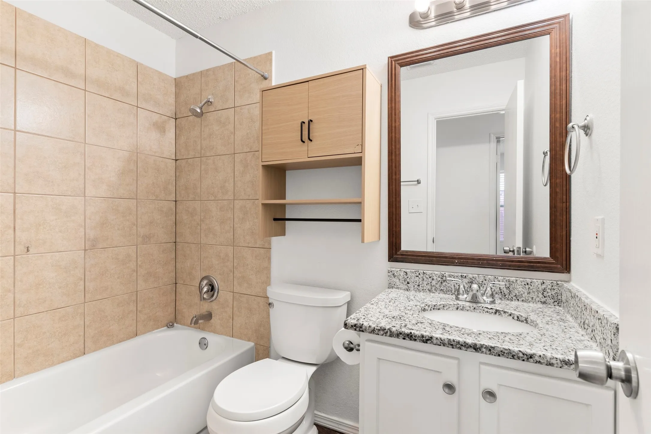 White vanity with a granite-style countertop, undermount sink, and wood-framed mirror