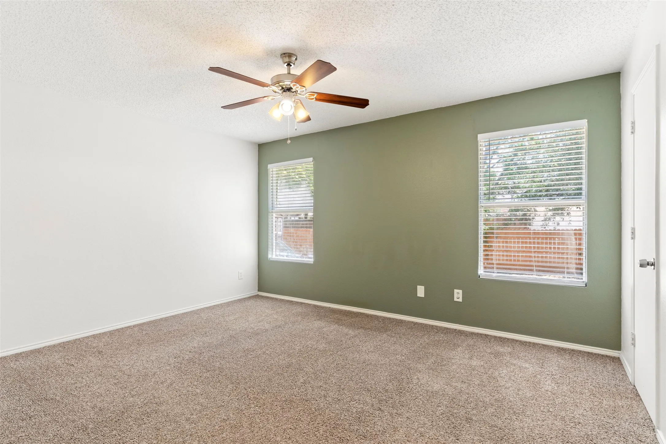 Textured carpeting, two windows with blinds, a ceiling fan, and a painted accent wall