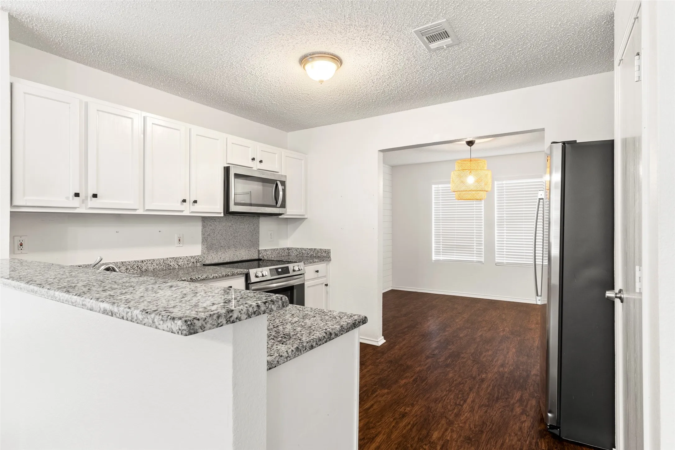 White cabinetry, gray speckled countertops, stainless steel microwave, black refrigerator, and wood-finish flooring