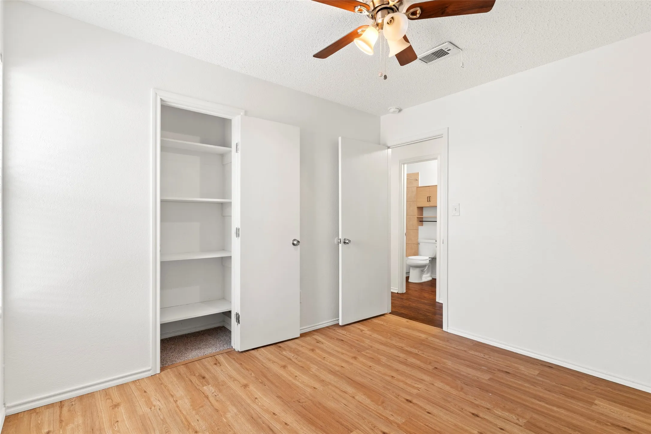 Wood-finish flooring, built-in shelving, white walls, and a ceiling fan with integrated lighting