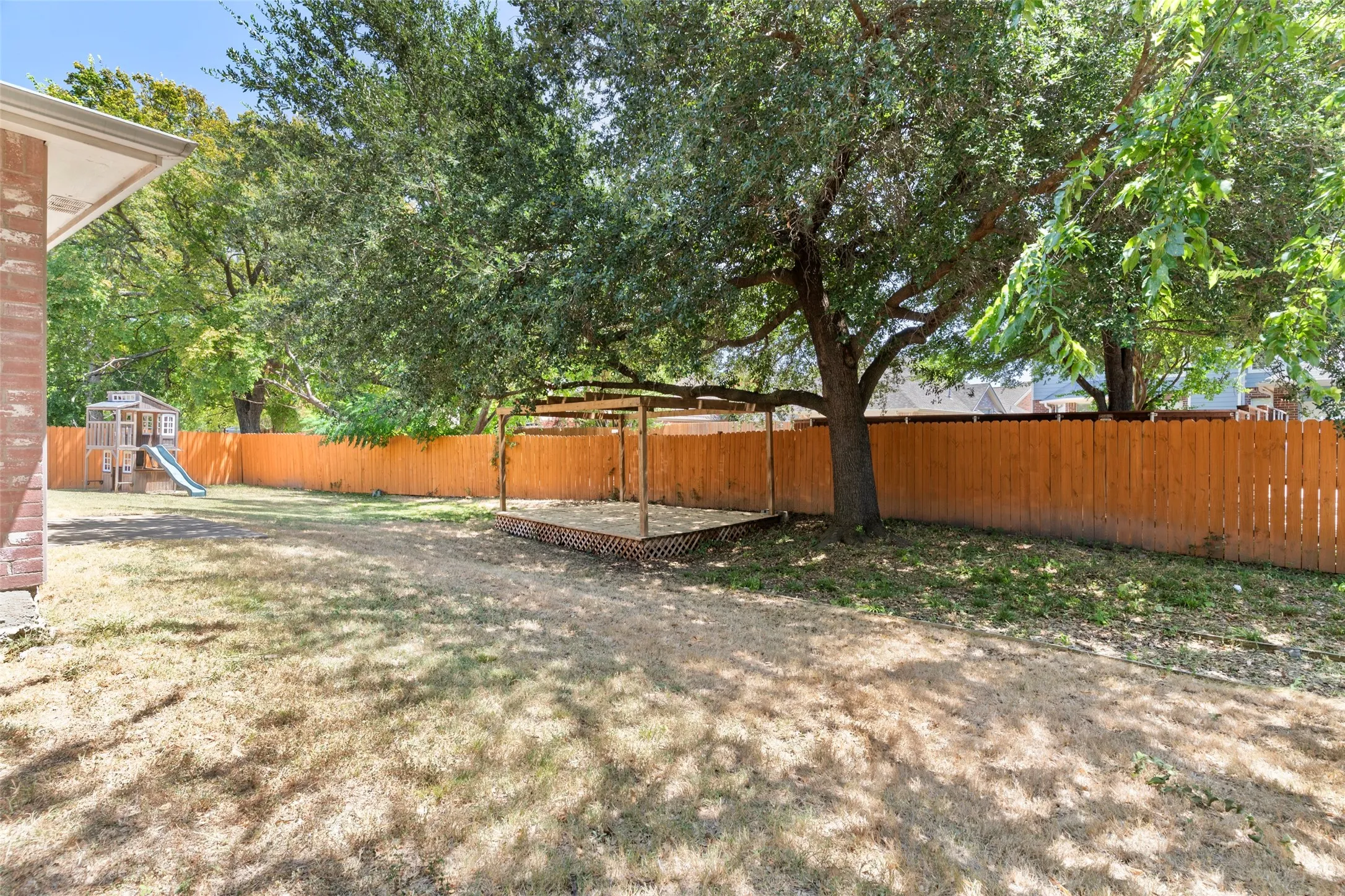 Fenced backyard with mature trees and a wood pergola structure