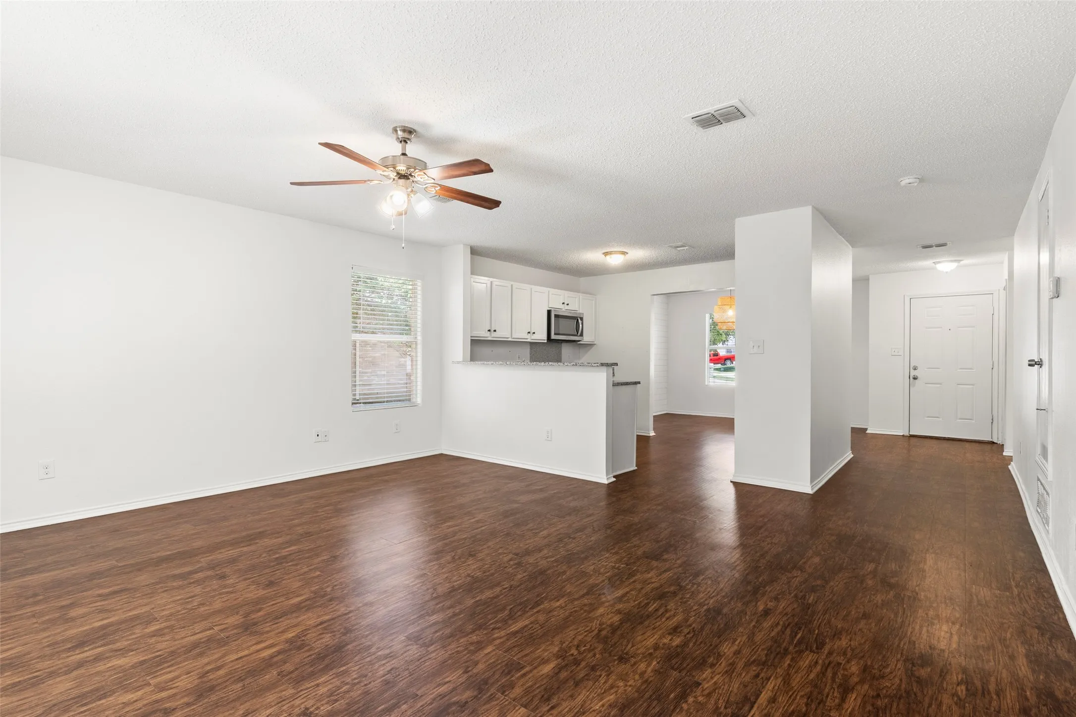 Open-concept living area featuring wood-finish flooring, a ceiling fan with light fixture, and white painted walls