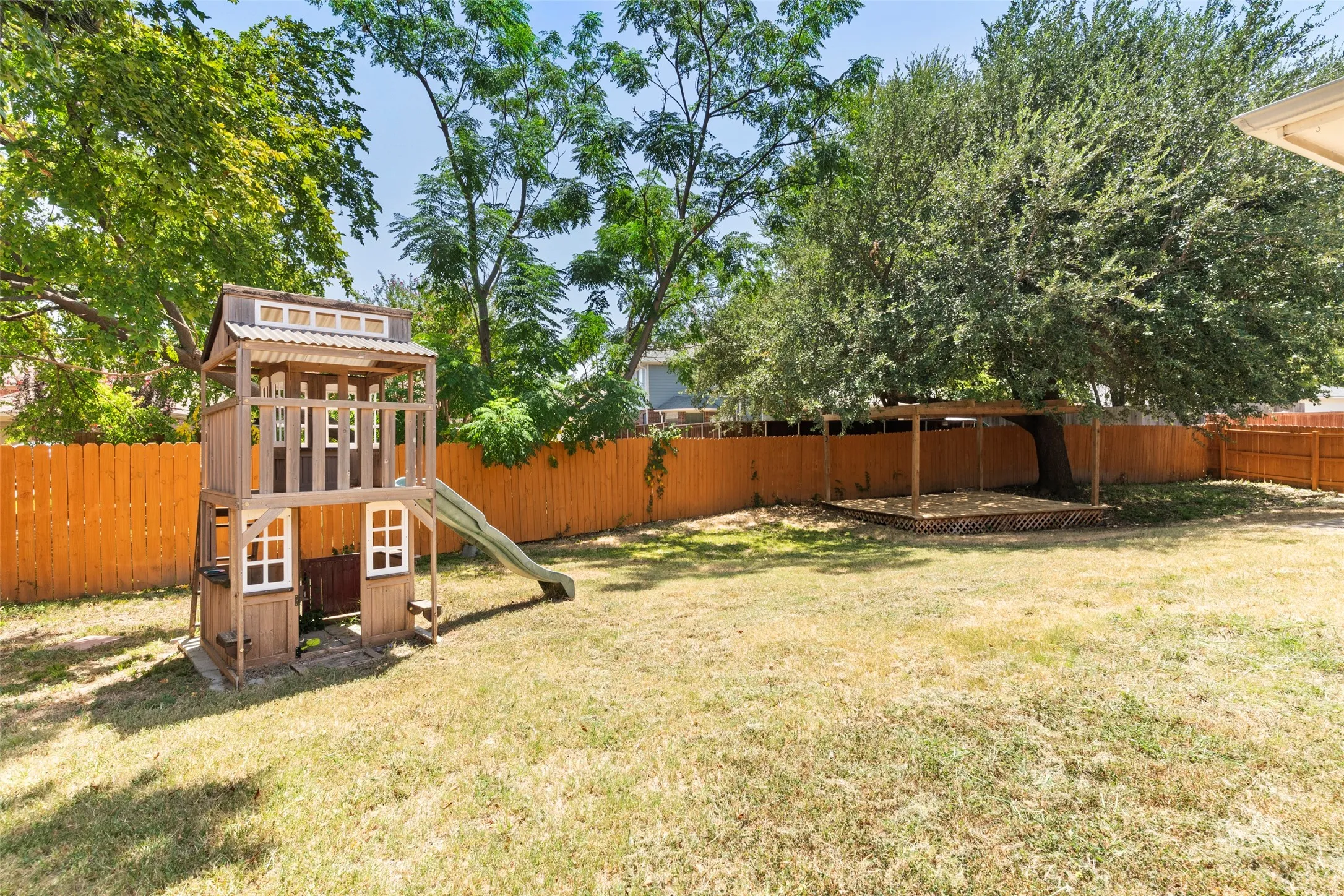 Expansive fenced yard with mature trees and a built-in wooden play structure