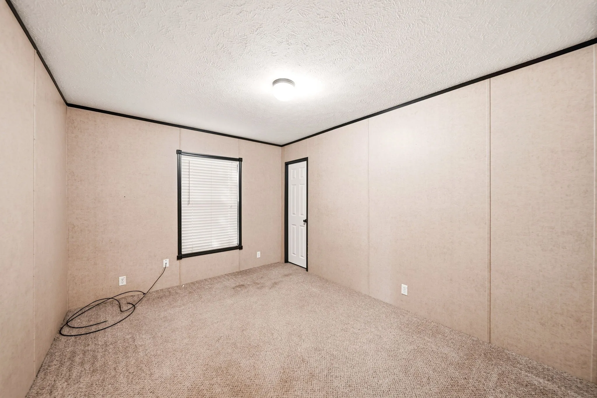 Textured wall panels, black trim accents, carpeted flooring, window with blinds, overhead lighting