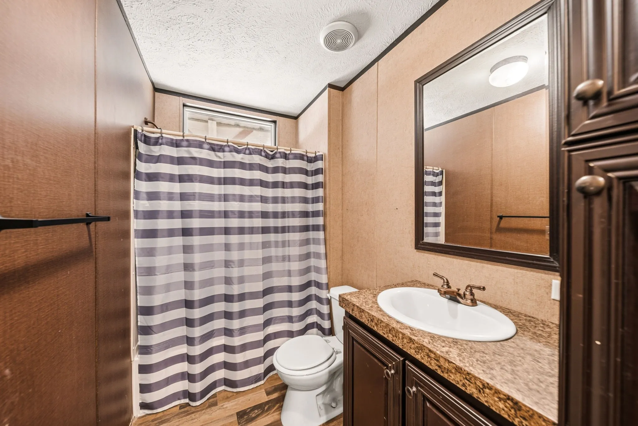 Bathroom featuring a single vanity with an oval sink, dark wood-finish cabinetry, a framed mirror, and wood-finish flooring