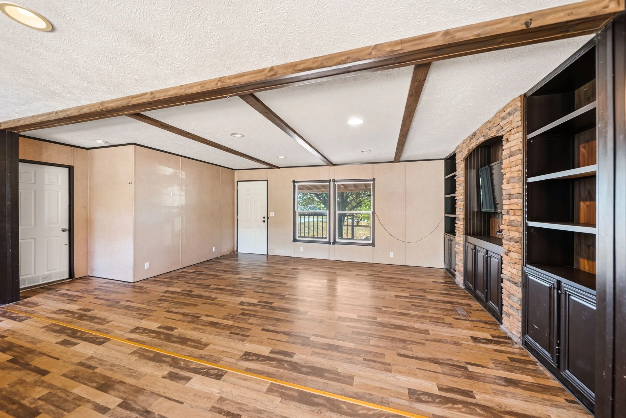 Wood-finish flooring, exposed ceiling beams, recessed lighting, built-in cabinetry, and a brick-accented entertainment wall